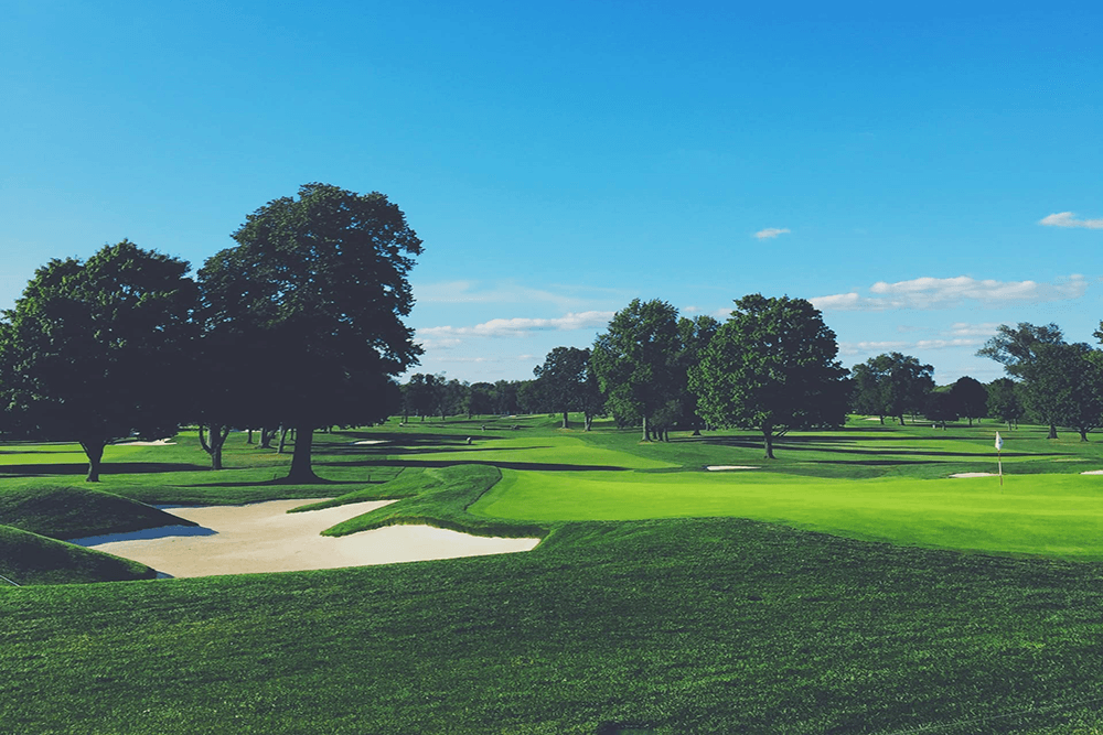 A scenic view of a golf course with green fairways, sand traps, and trees under a clear blue sky.