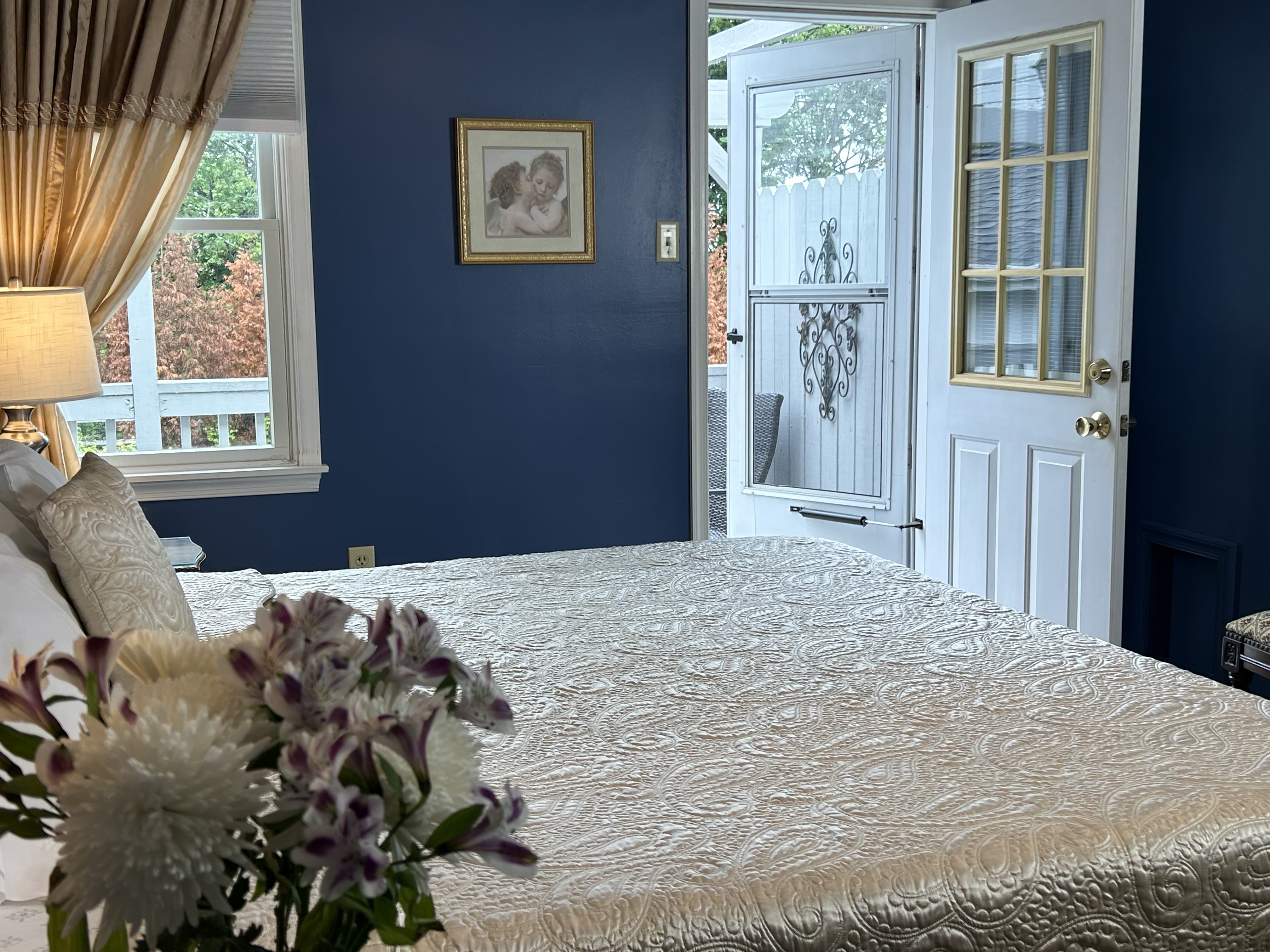 Side view of king bed with night tables, lamps, flowers, a window and door open to balcony