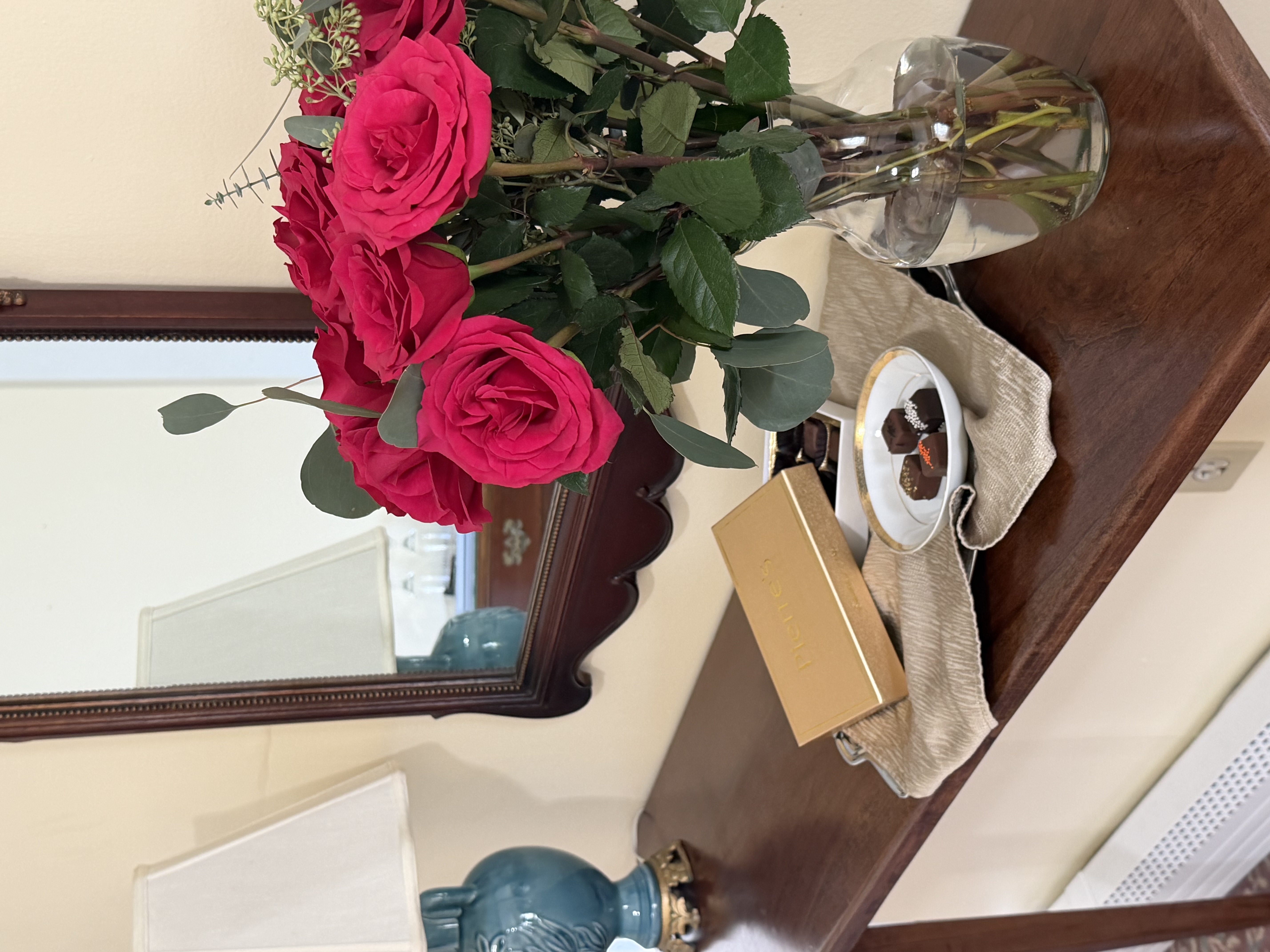 Flowers & chocolates on table by mirror & lamp