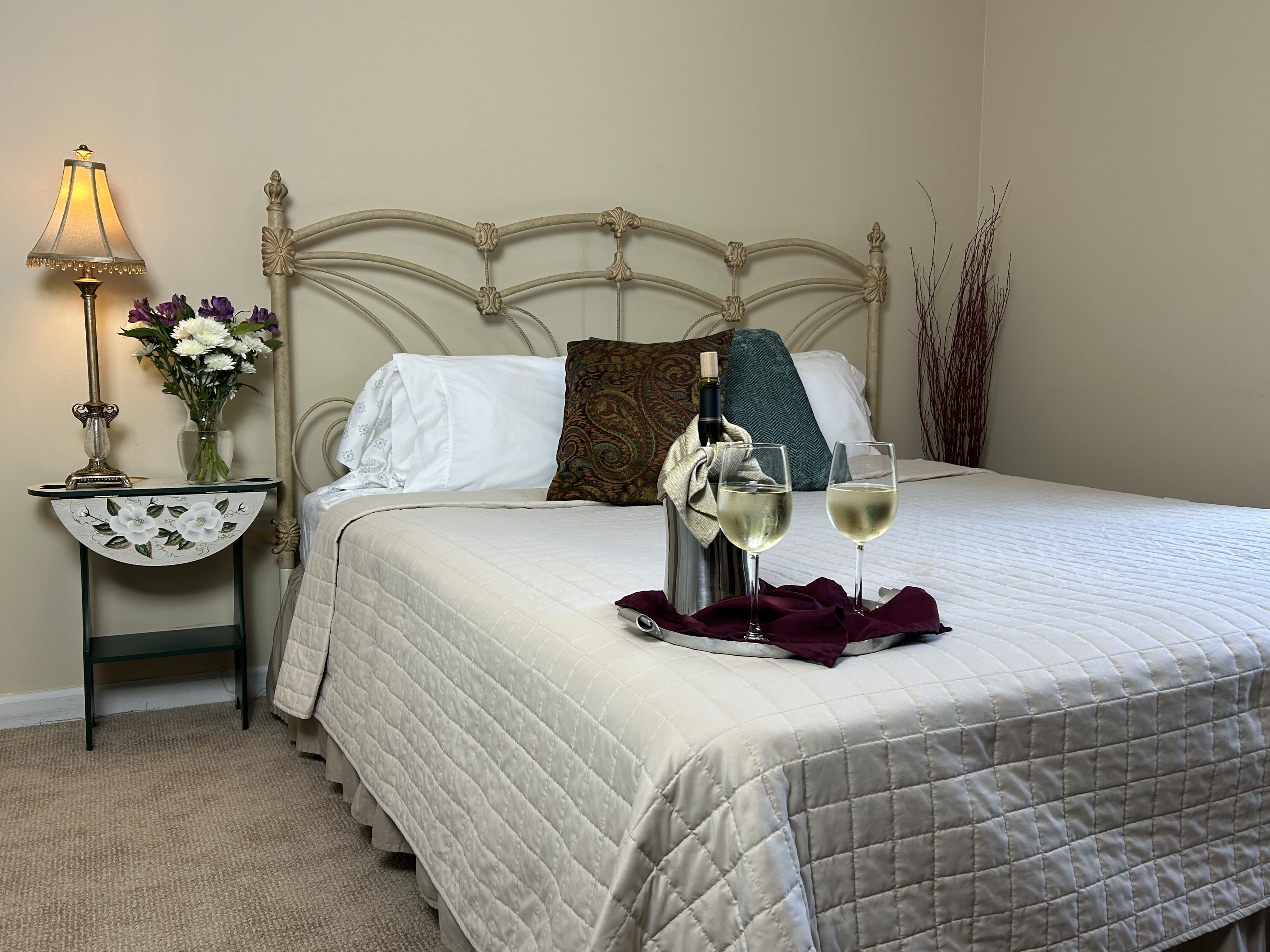 View of king bed, side table & lamp with tray of white wine & glasses