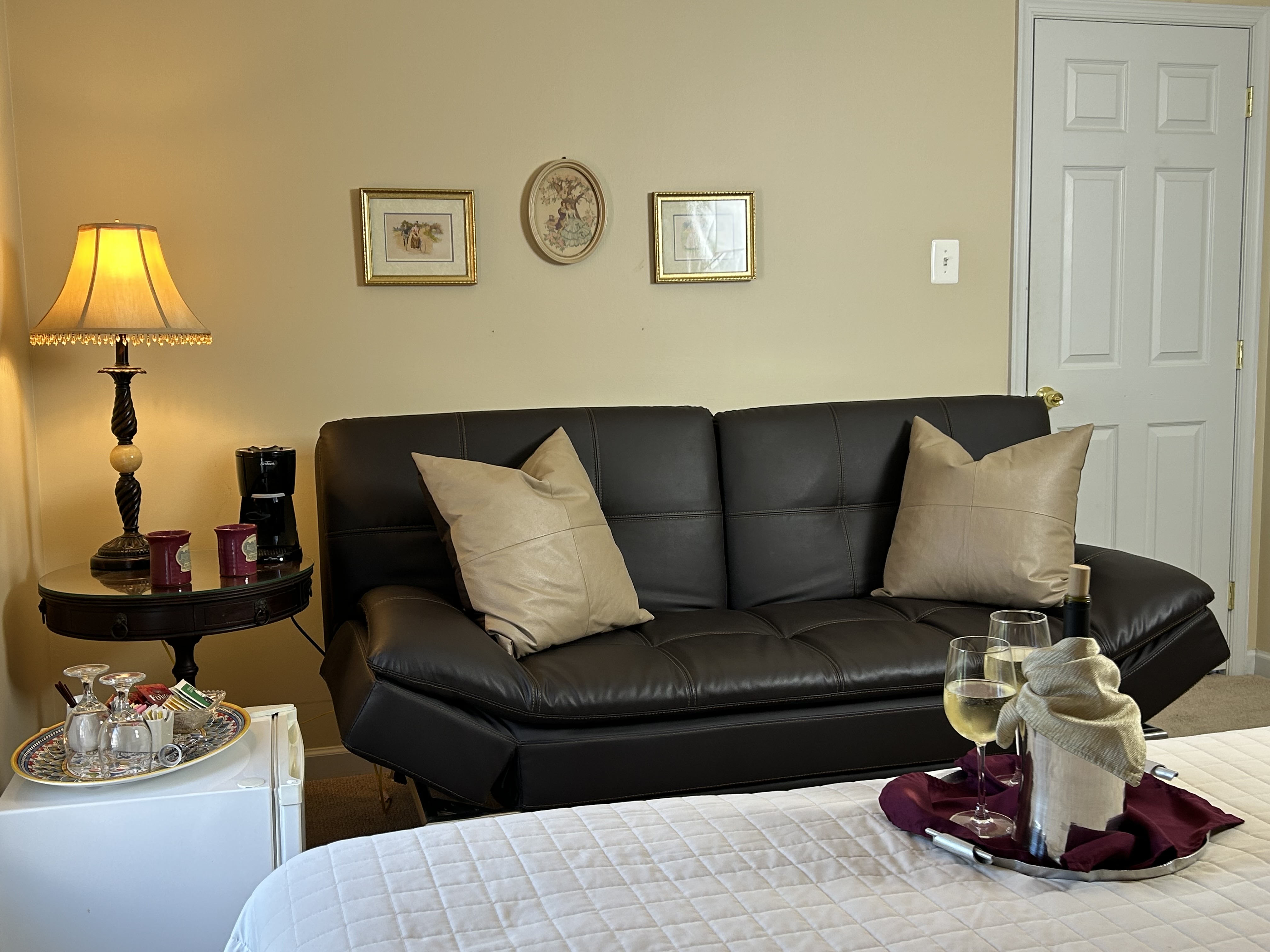 View of sitting area with couch, side table,lamp & mini fridge with amenities