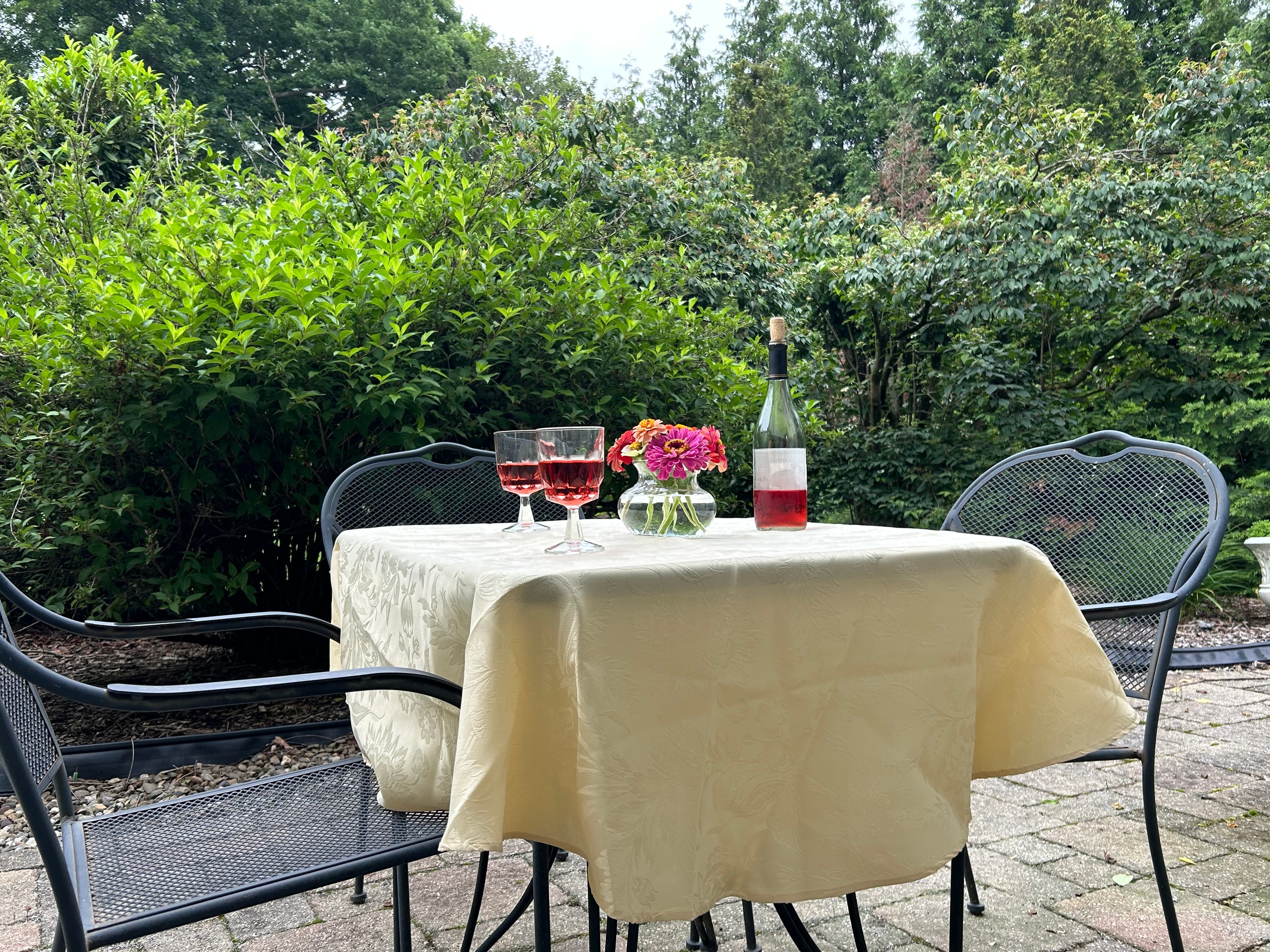 View of back patio with table and chairs, wine 2 wine glasses and flowers overlooking rear garden