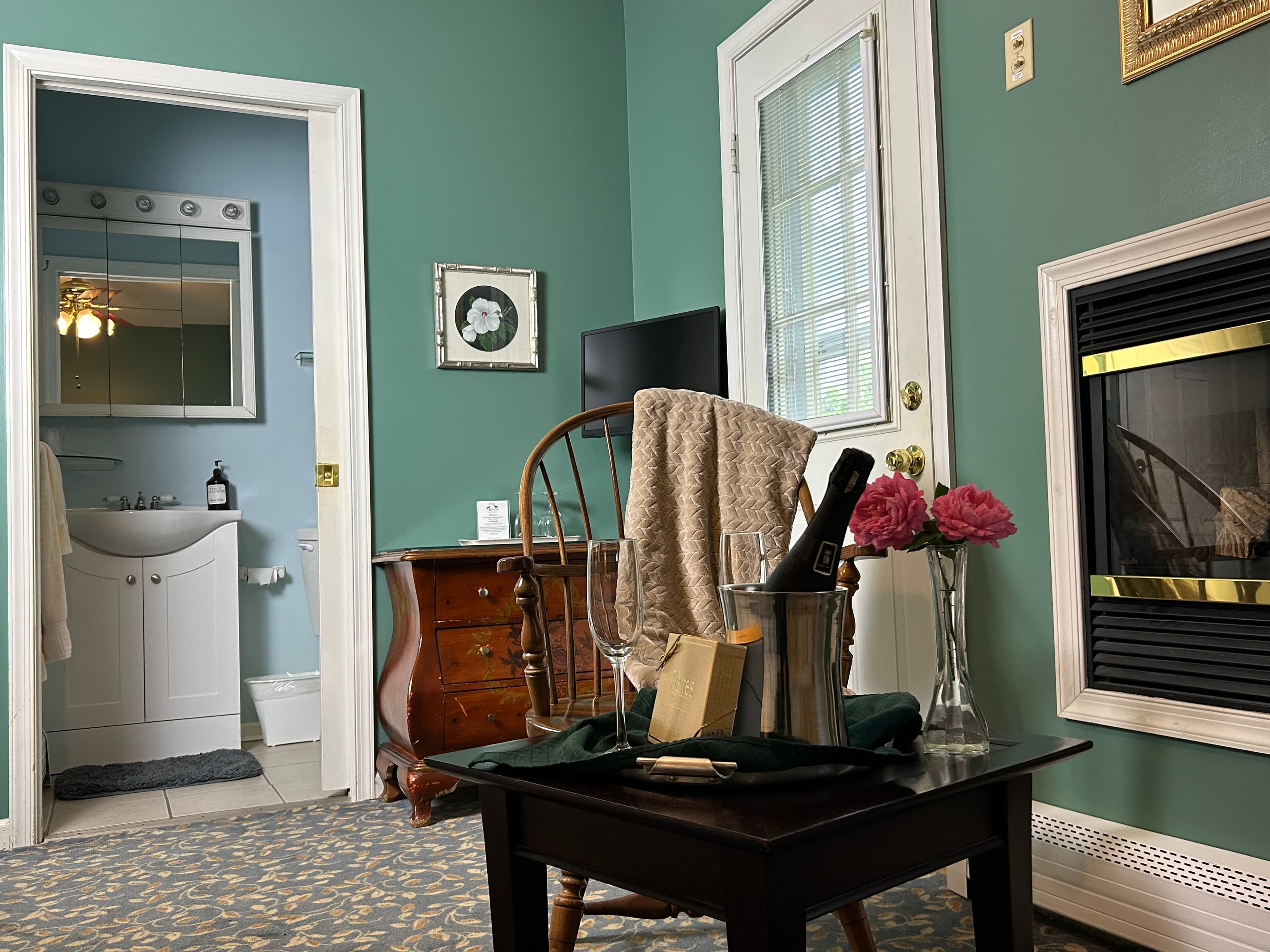 View of backdoor patio closed. TV, dresser and bathroom with chair and table in foreground