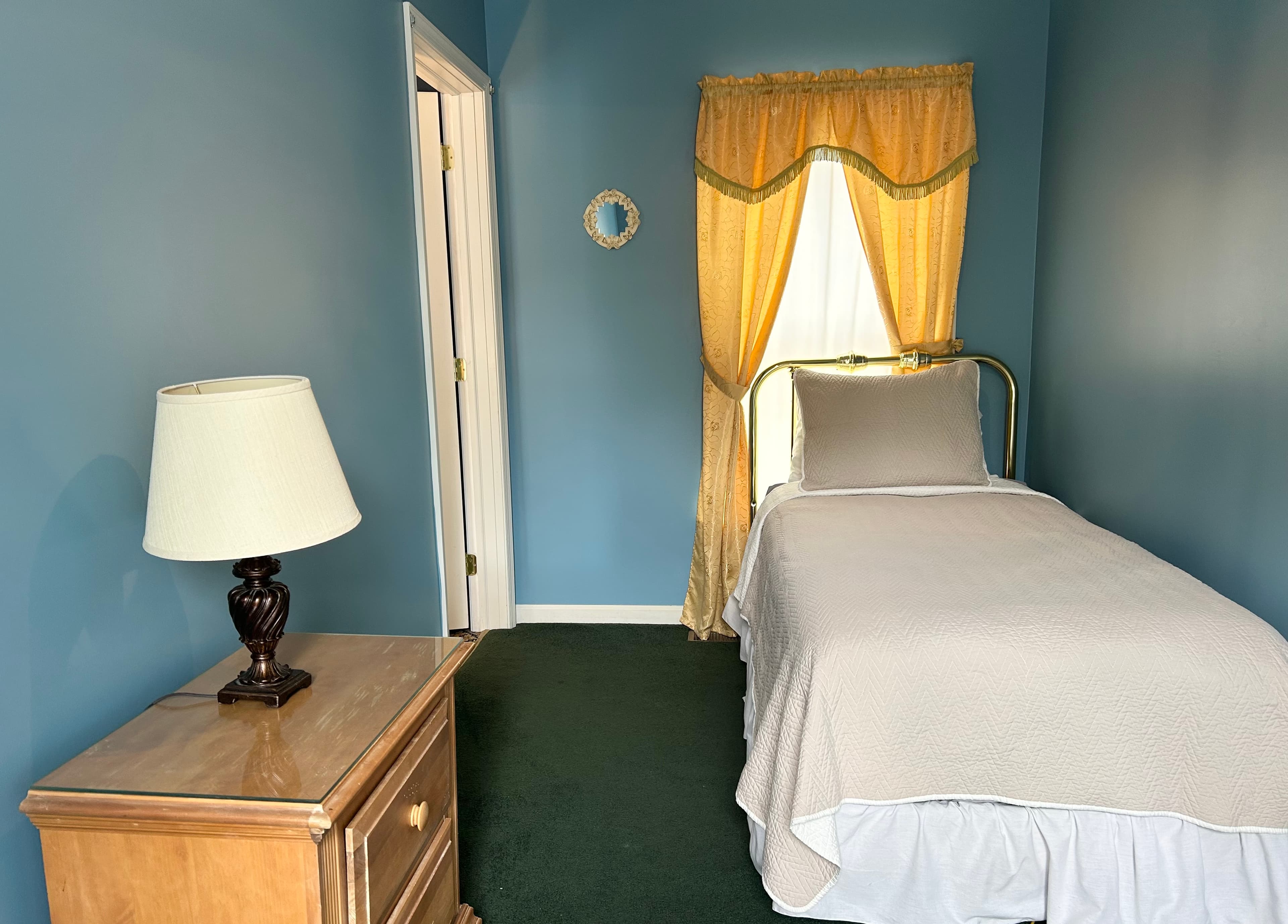View of twin bed, night table with lamp and window in adjunct room