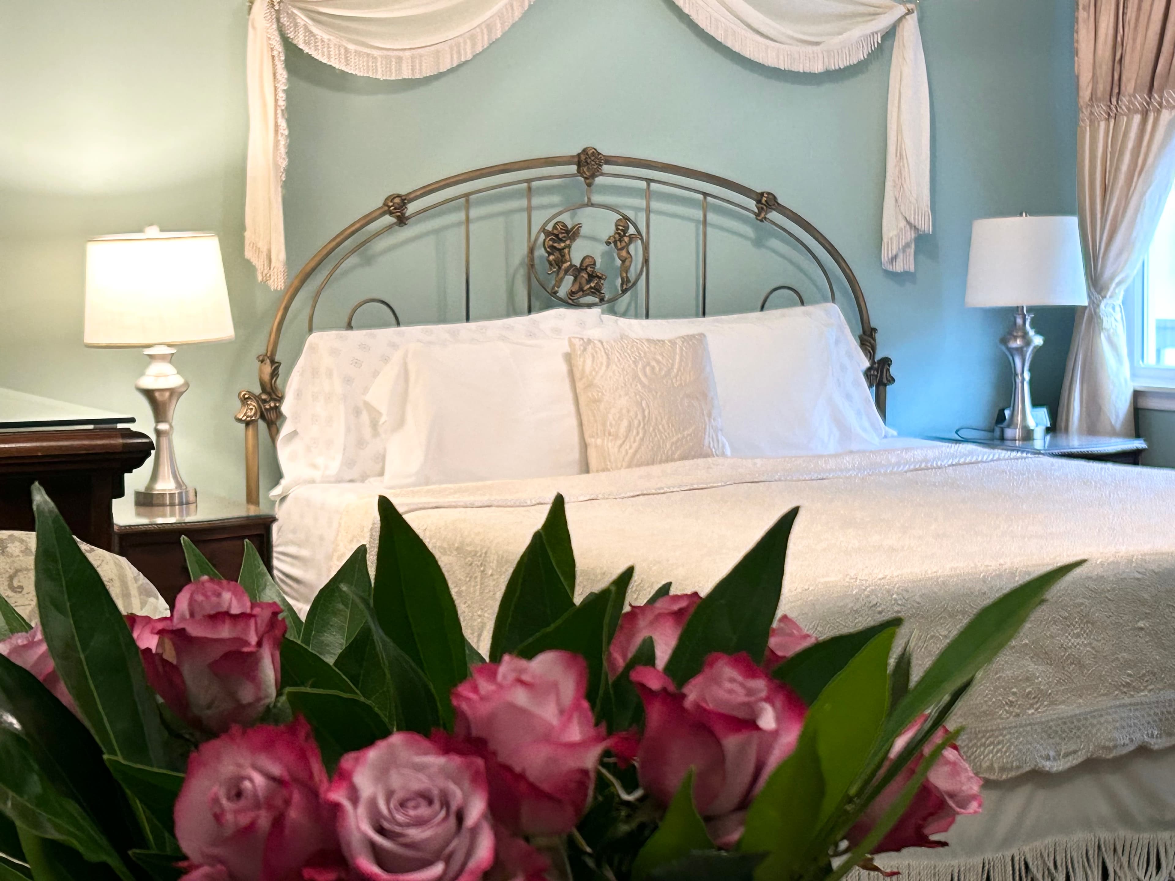 Bouquet of flowers in foreground with king bed, night tables and window in background