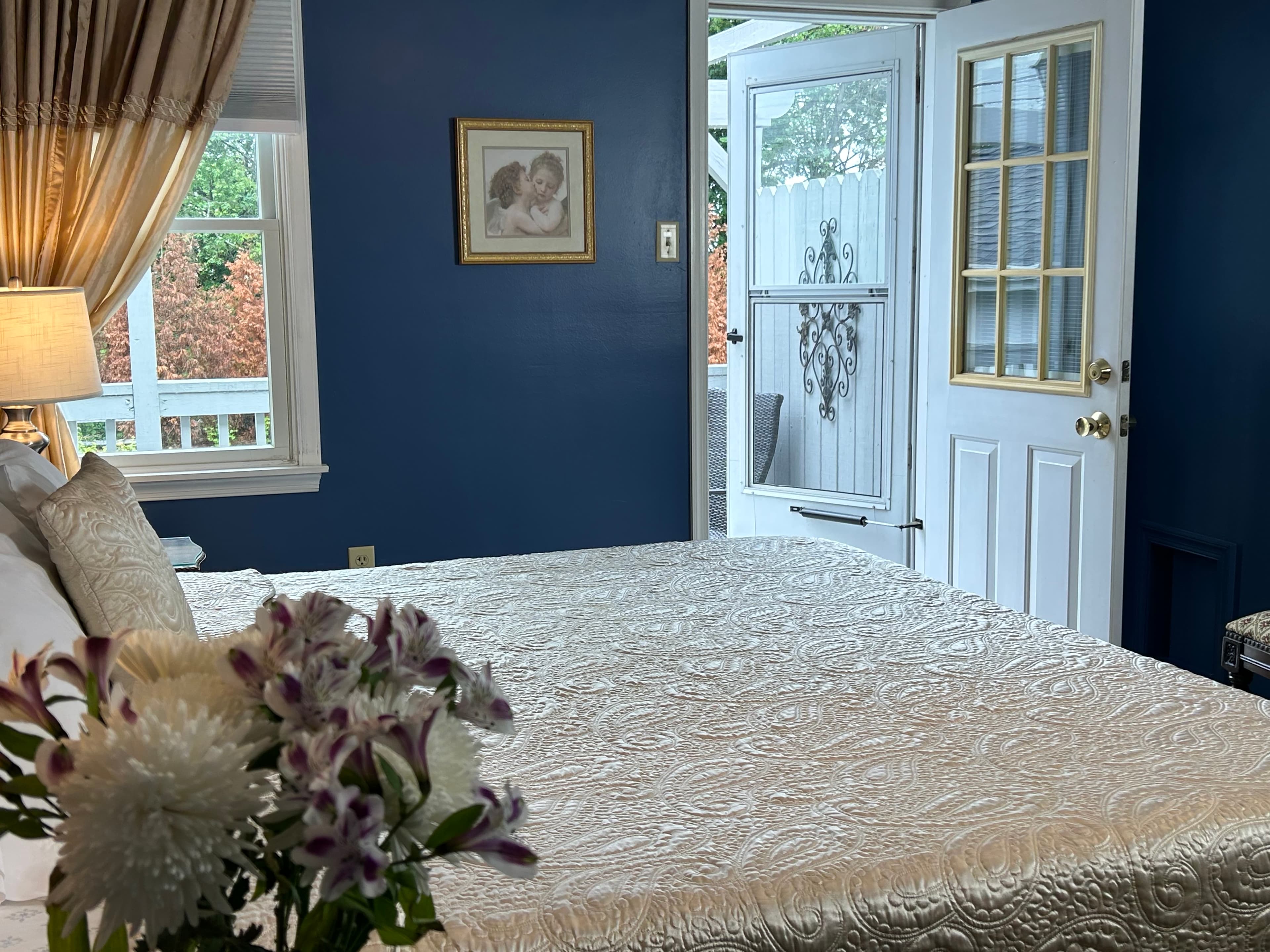 Side view of king bed with night tables, lamps, flowers, a window and door open to balcony