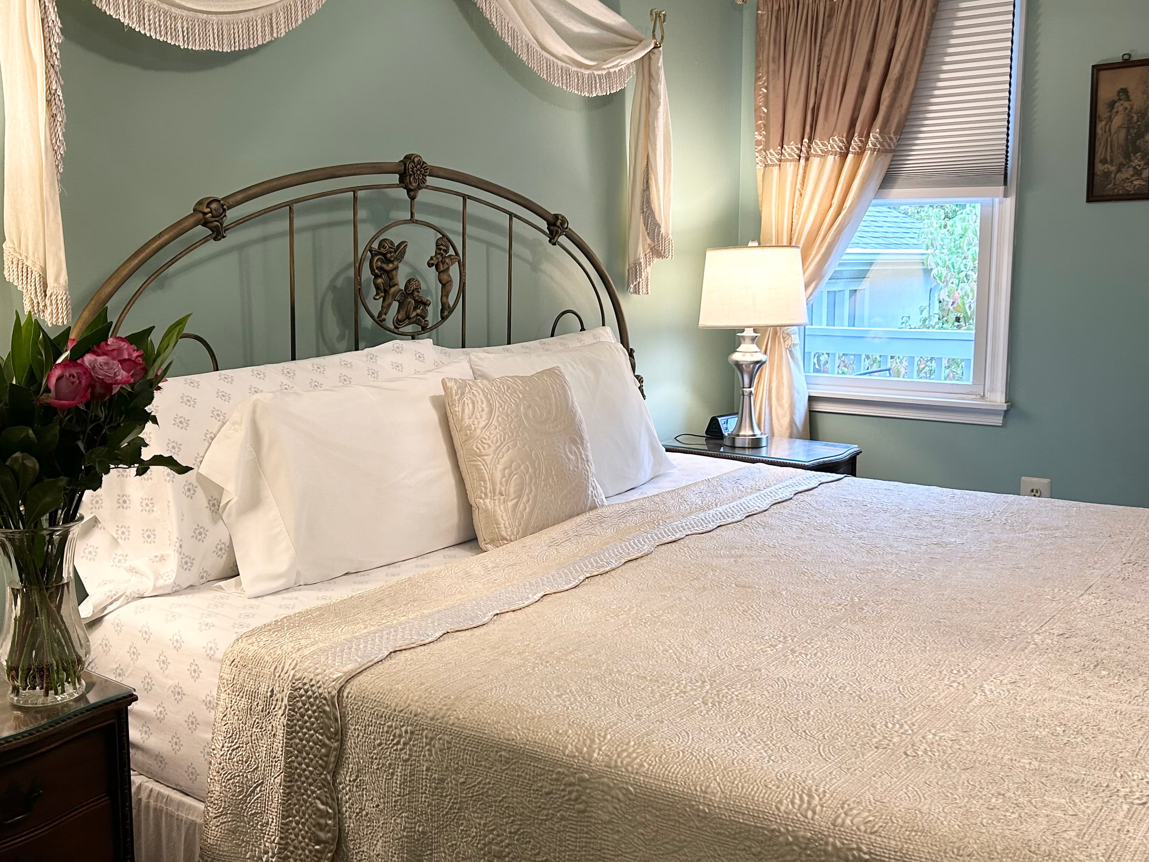 Side view of king bed with night tables, lamps, flowers and a window