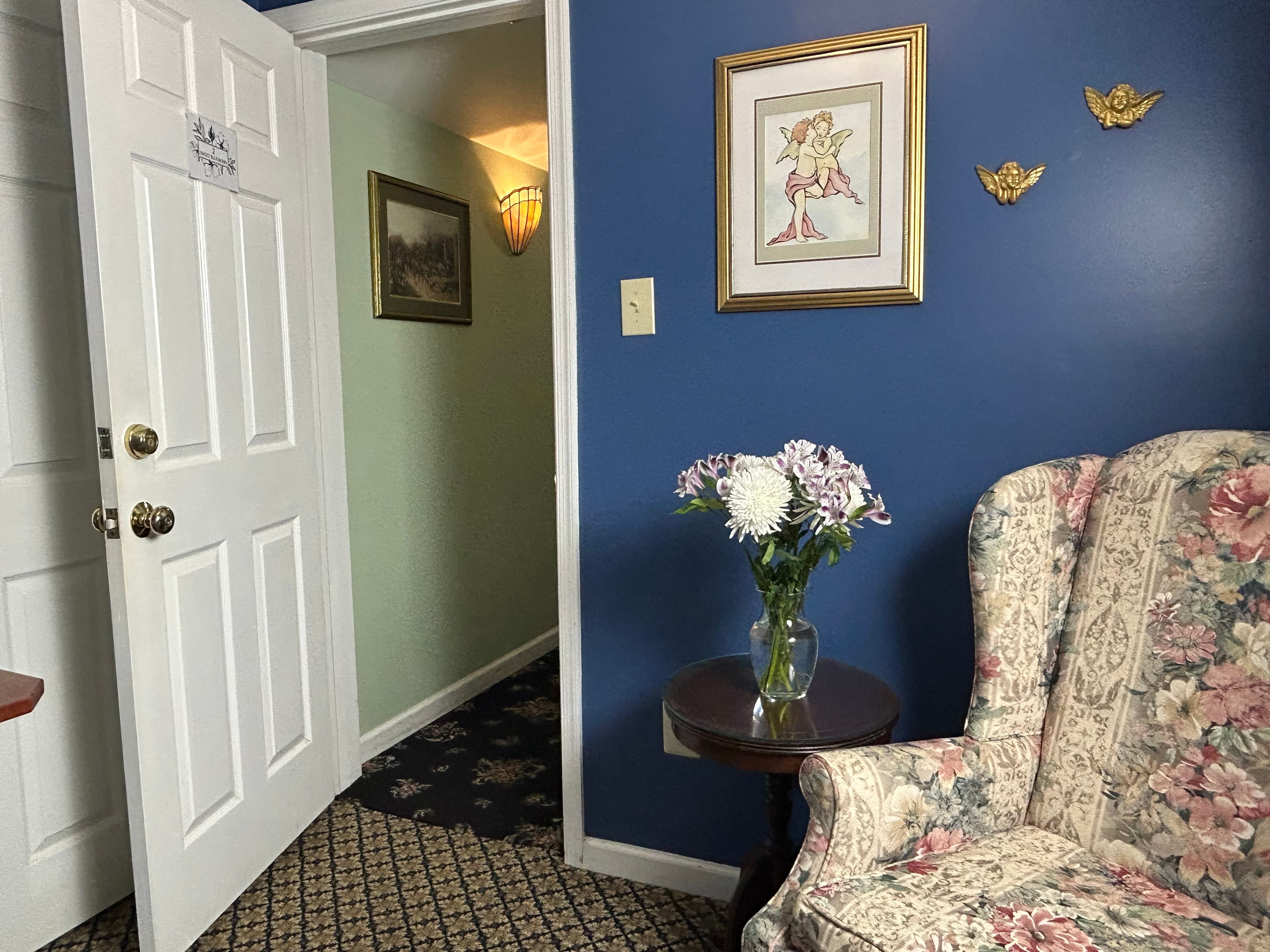 View of high back chair with side table and flowers by open front doo
