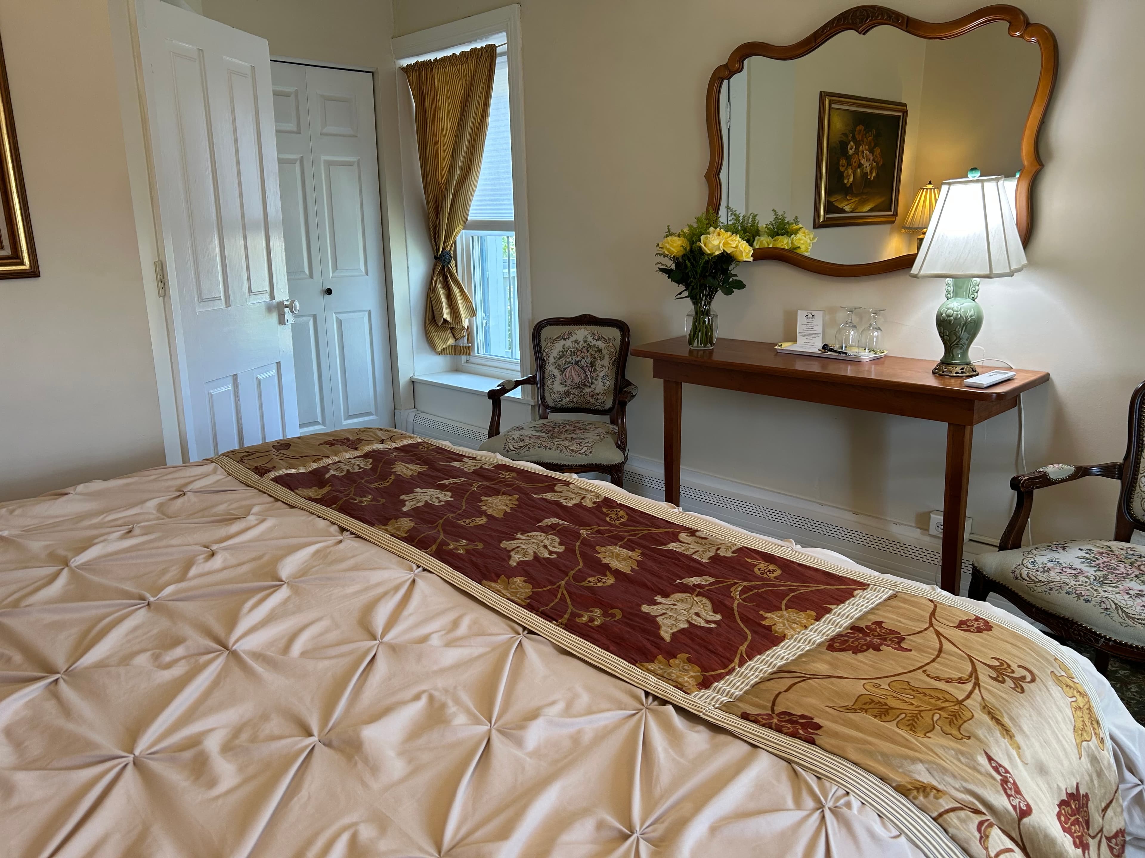 View of end of king bed, 2 chairs. a window and a mirror over side table