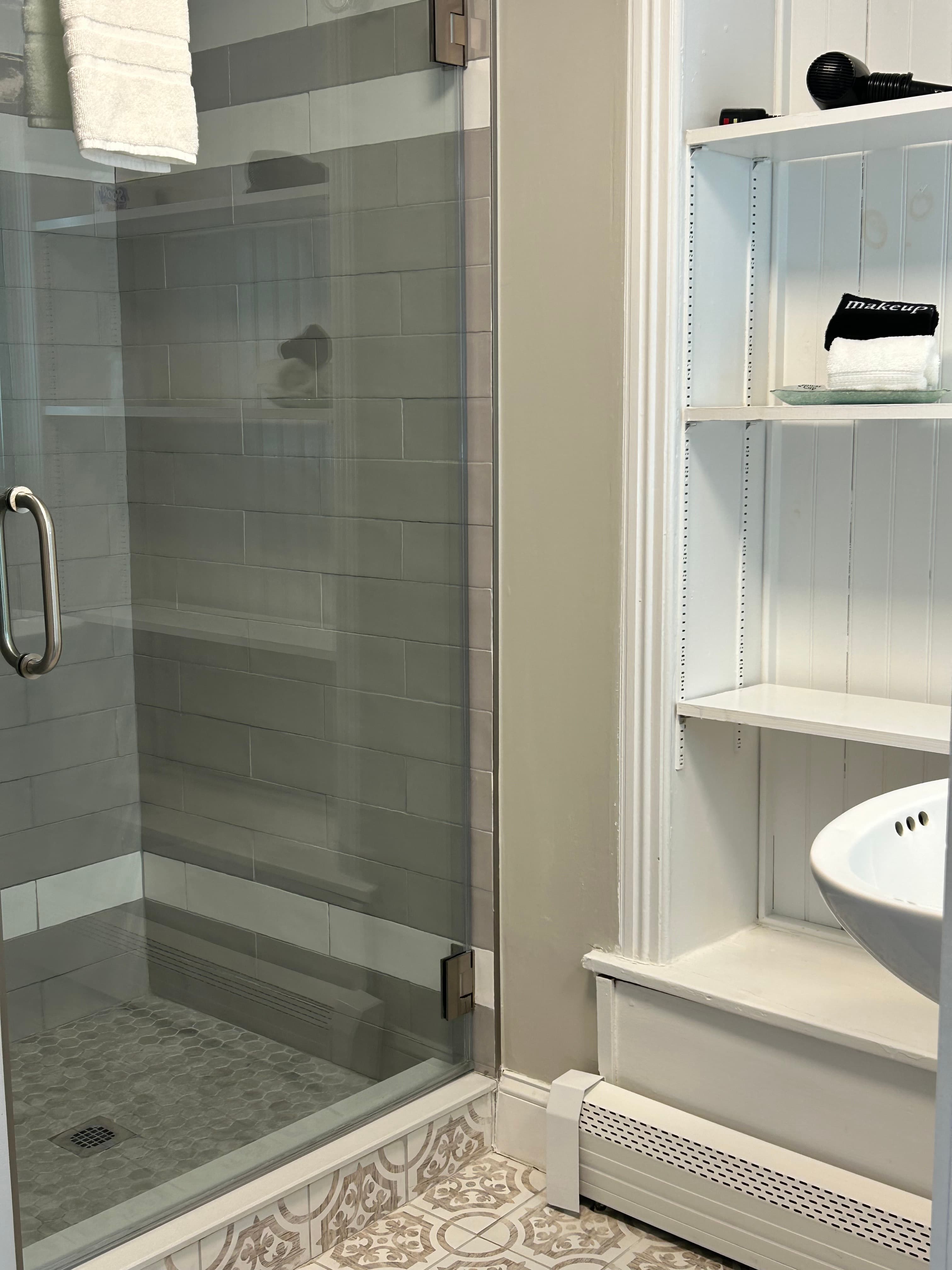 Looking into the bathroom with a glass door tile shower and wood shelves