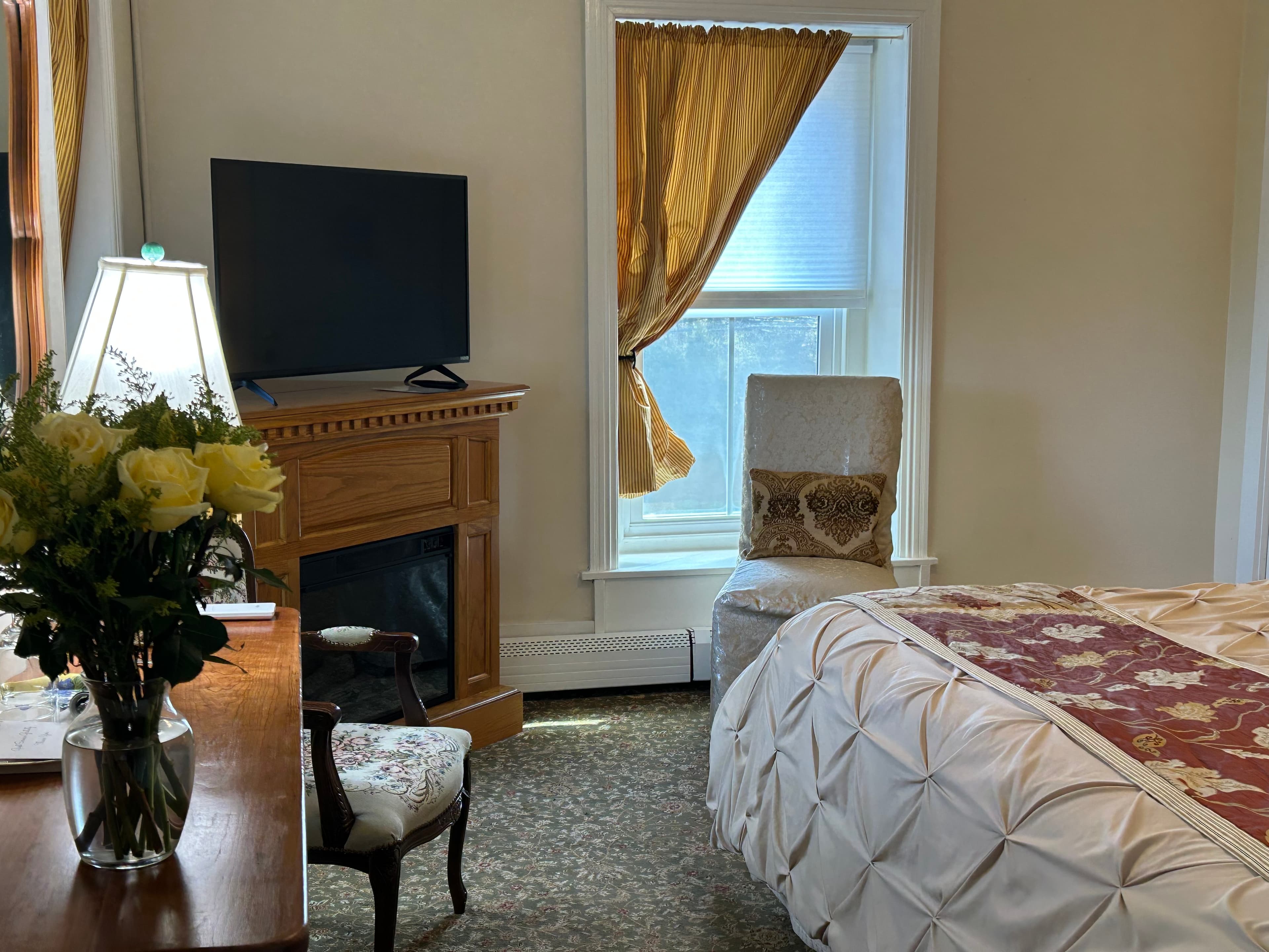 Flat screen TV on an electric fireplace by a window and chair