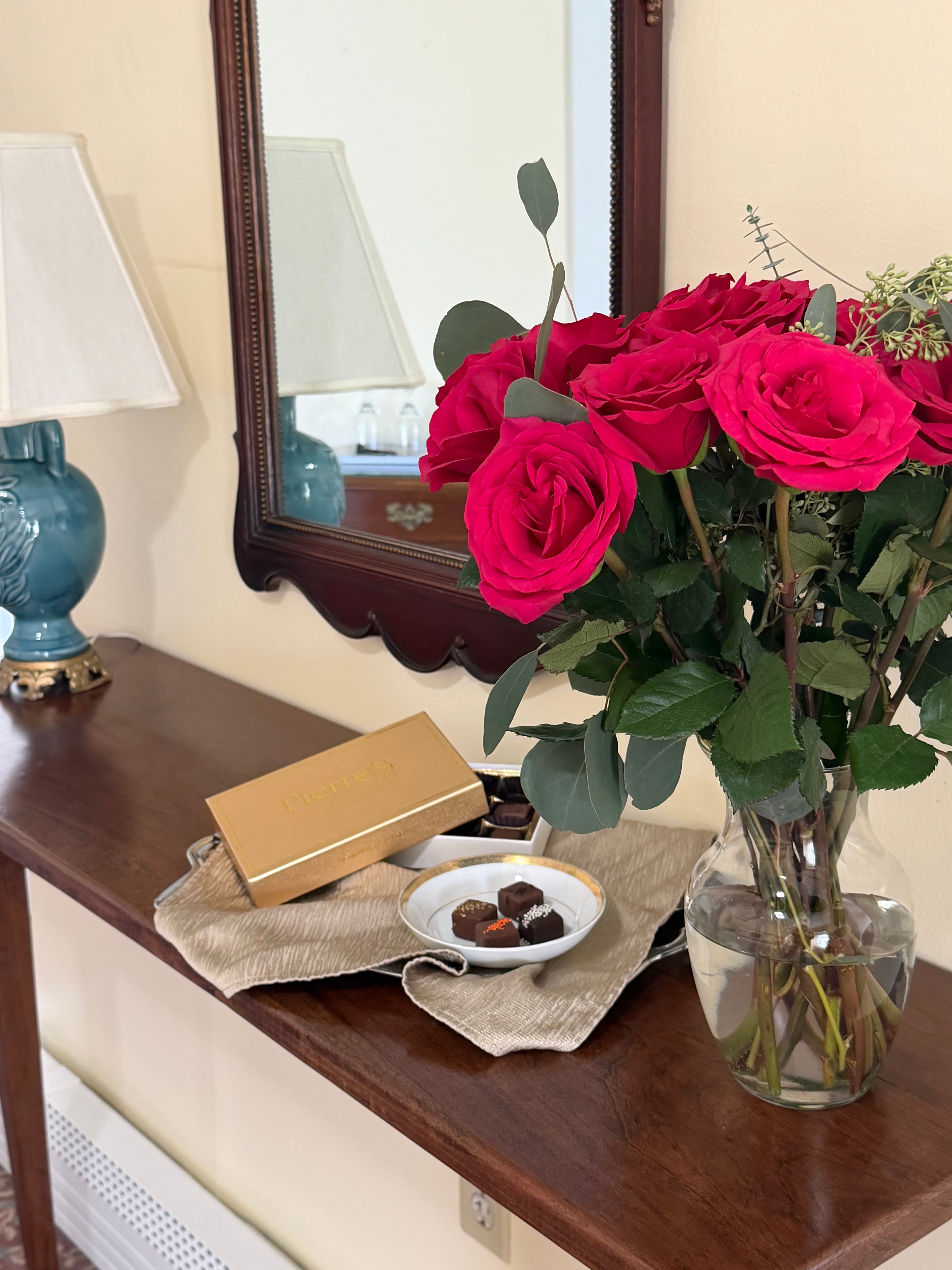 Flowers & chocolates on table by mirror & lamp