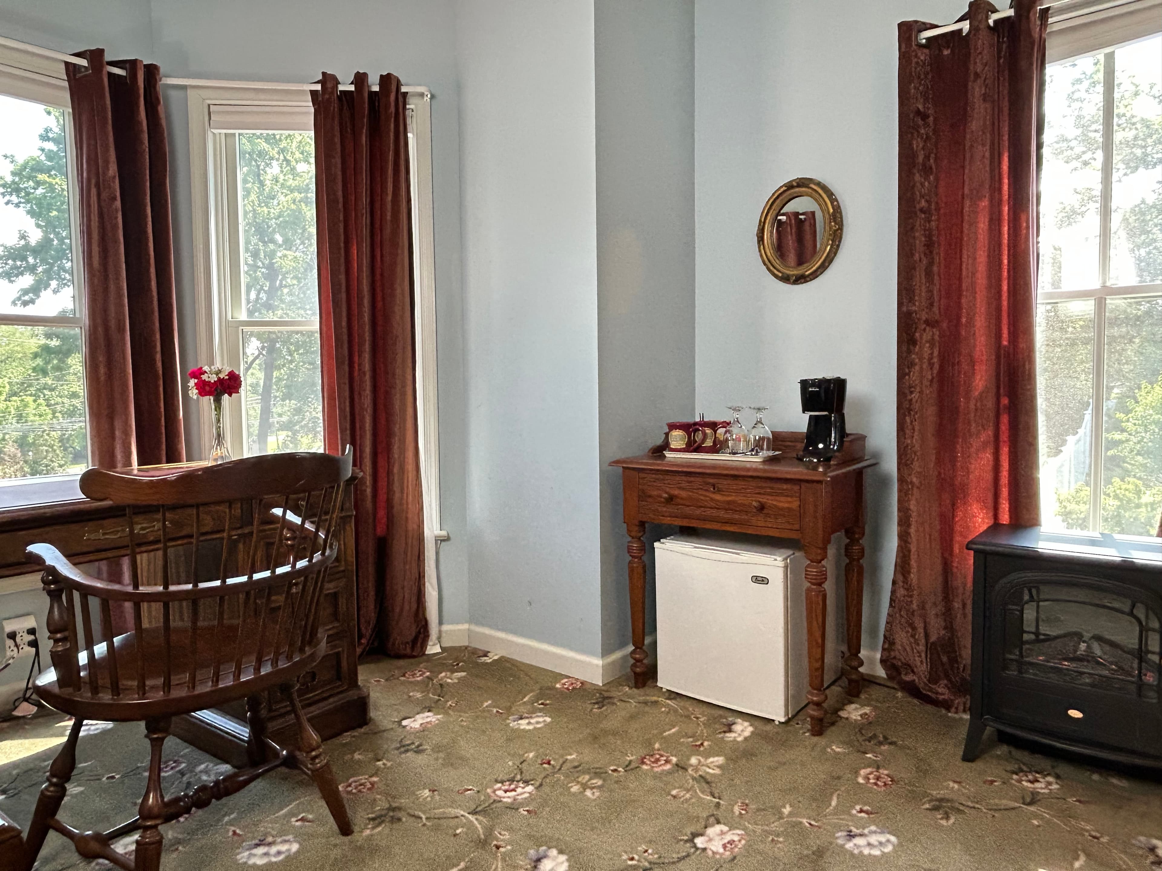 View of bay windows, desk & chair, mini fridge & electric fireplace
