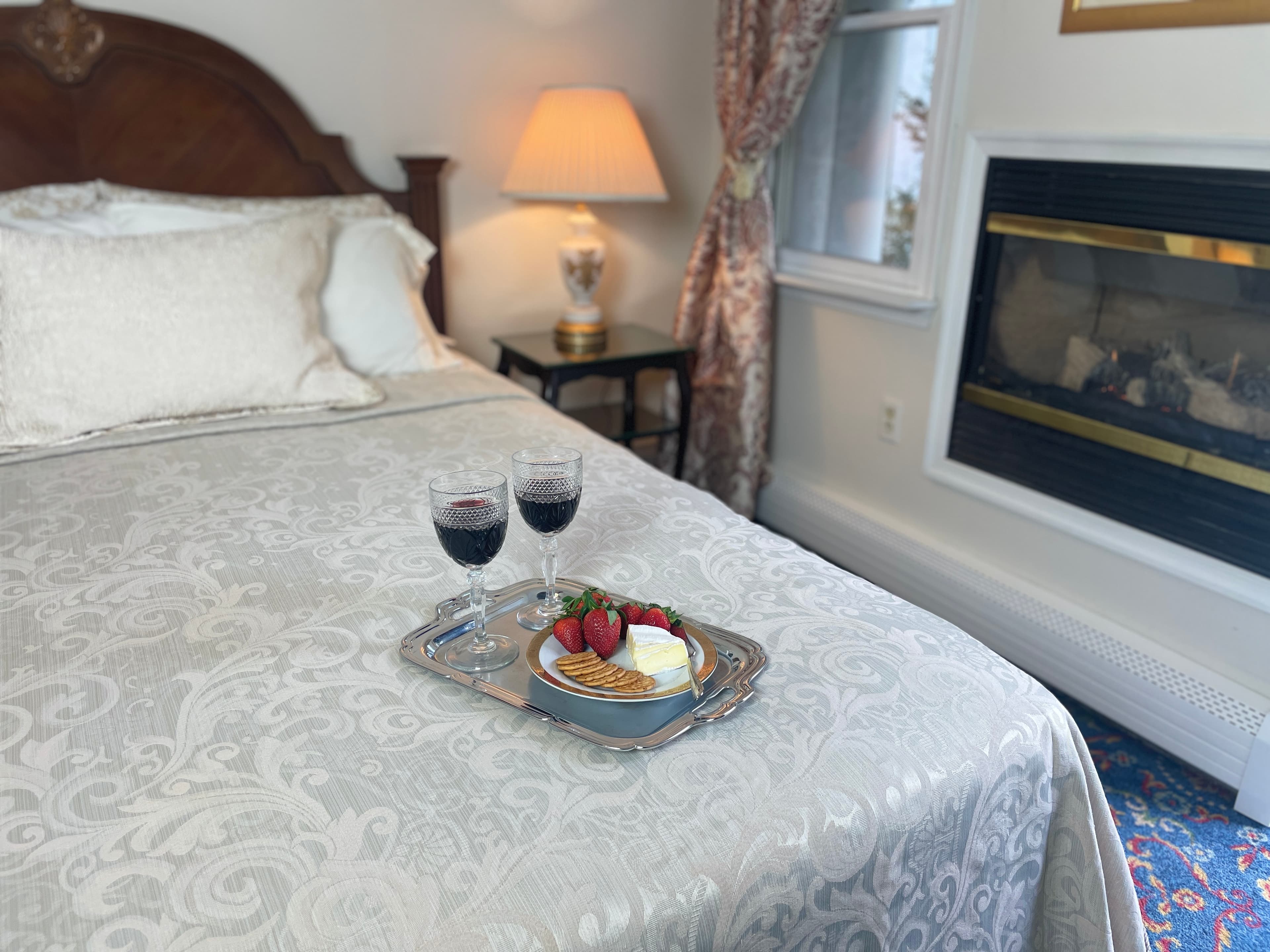 view of bed and side table with lamp and tray of wine and strawberries and cheese