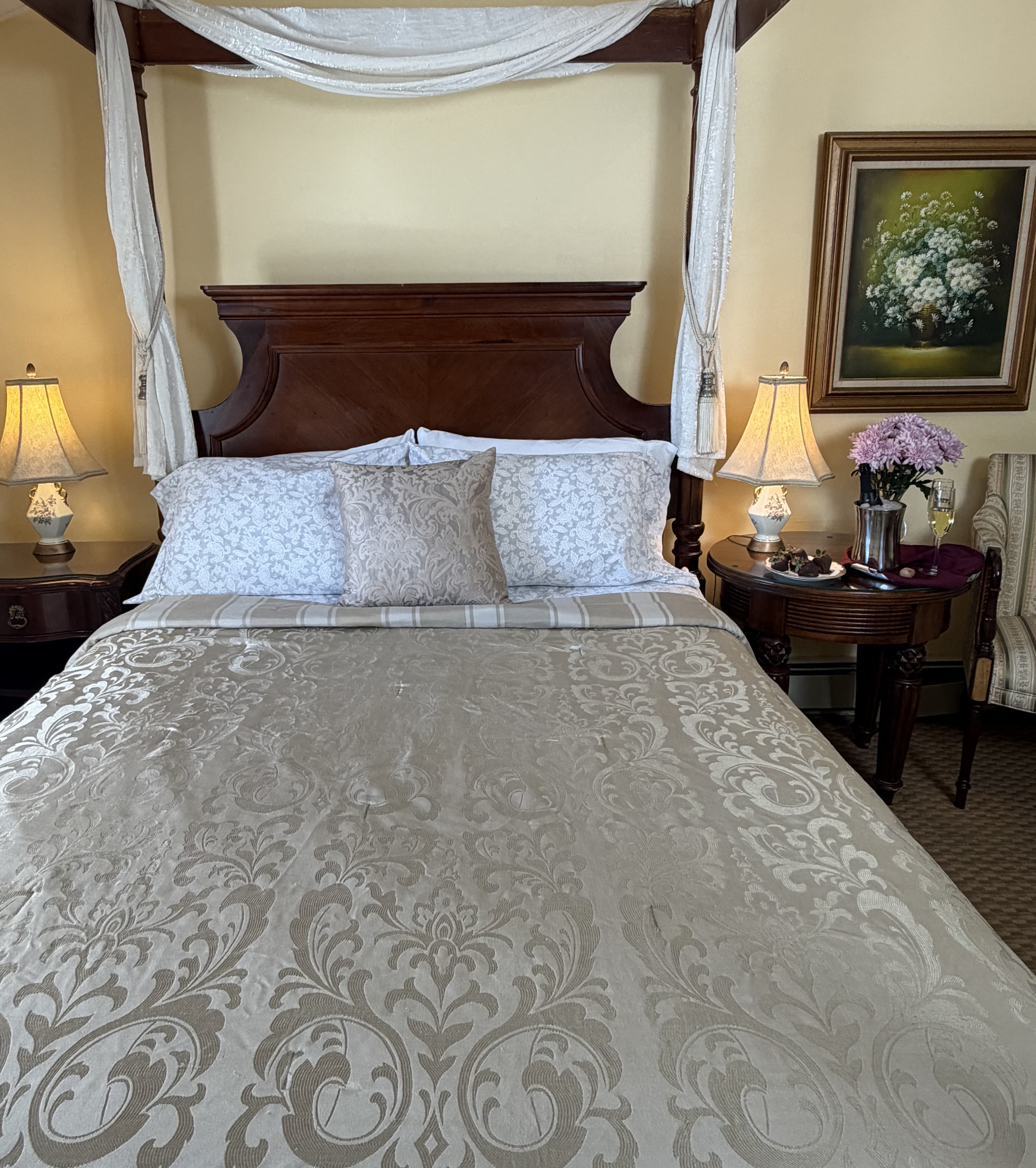 Front view of 4-post walnut queen bed with side table & chair, champagne & flowers