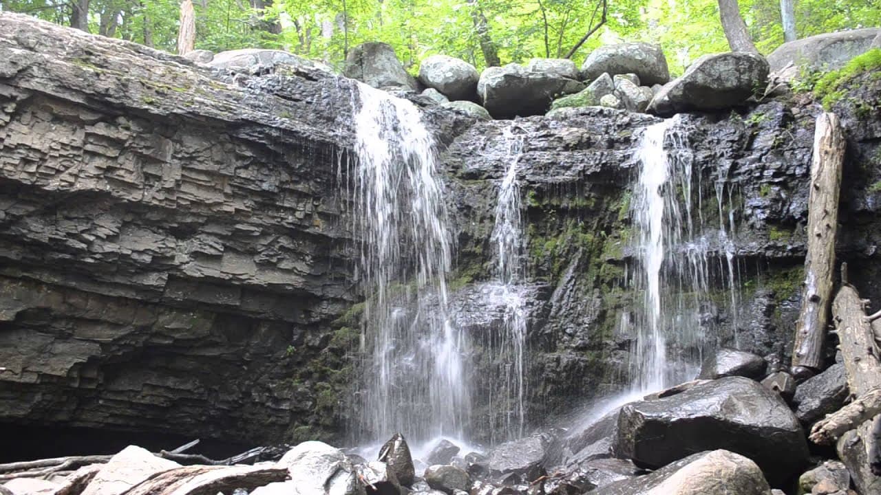 A serene waterfall cascades over rocky terrain, surrounded by lush green trees.