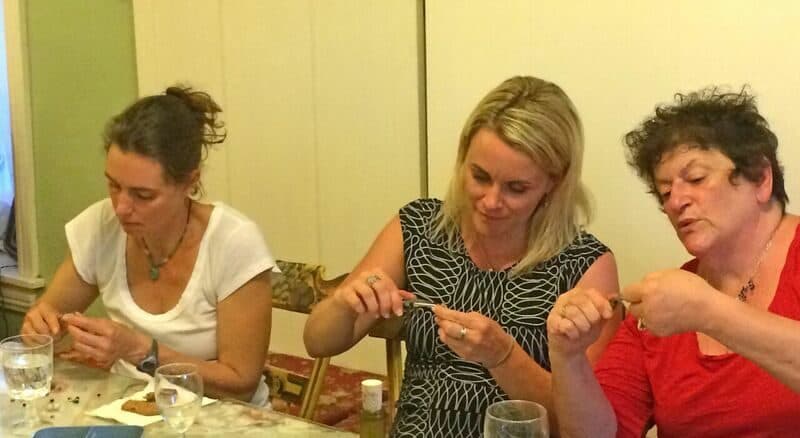 Three women engaged in a craft activity at a table, focusing on their hands.