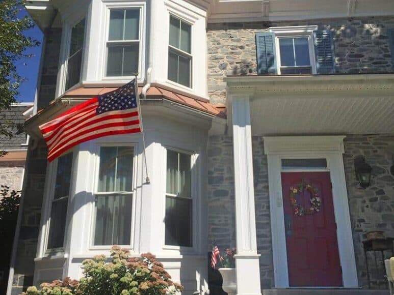 A historic stone house with a red door and an American flag hanging outside.