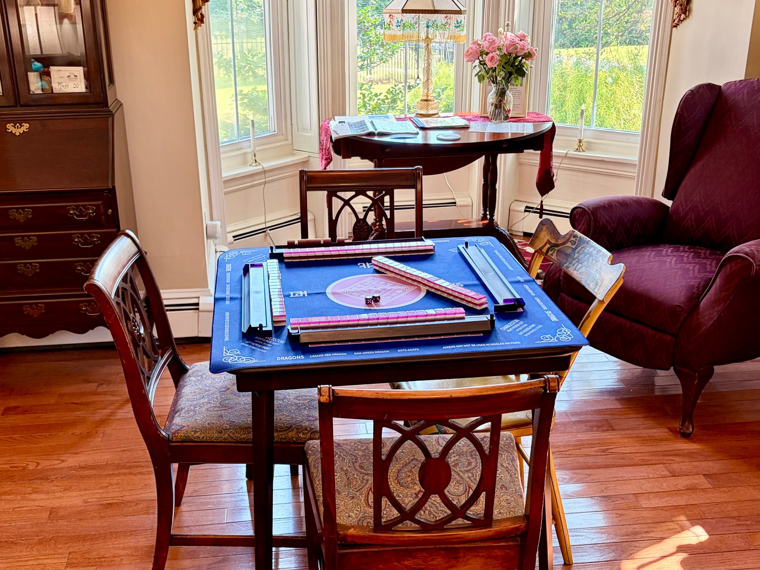 A cozy game table set up with mahjong tiles and surrounded by wooden chairs in a well-lit room.