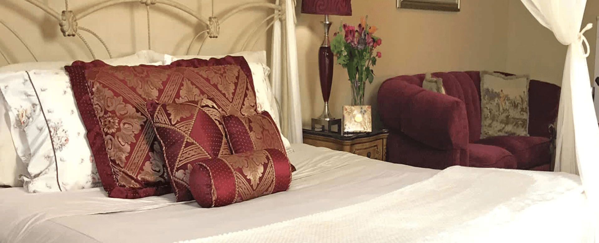 A cozy bedroom featuring a decorative bed with patterned pillows and a plush red sofa.