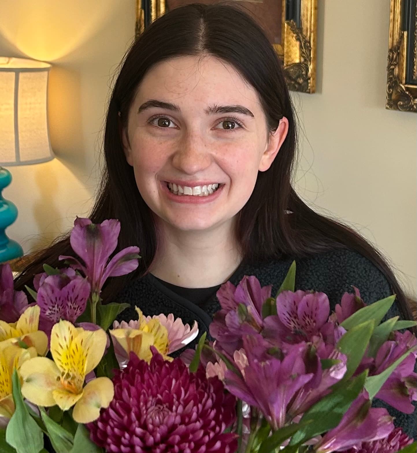 A young woman smiles broadly while surrounded by vibrant flowers.