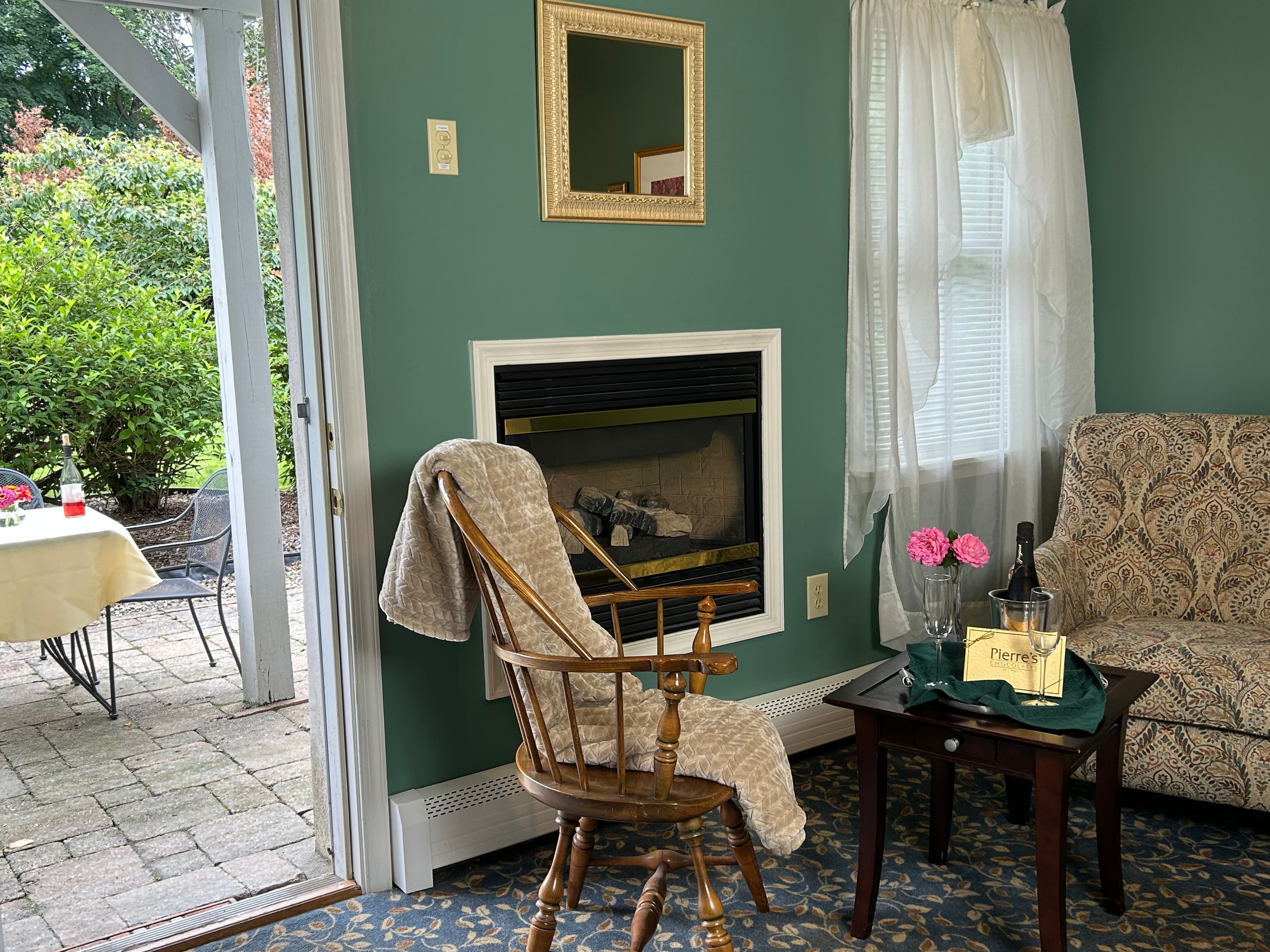 A cozy living space featuring a rocking chair, a fireplace, and a small table with a champagne bottle and flowers.