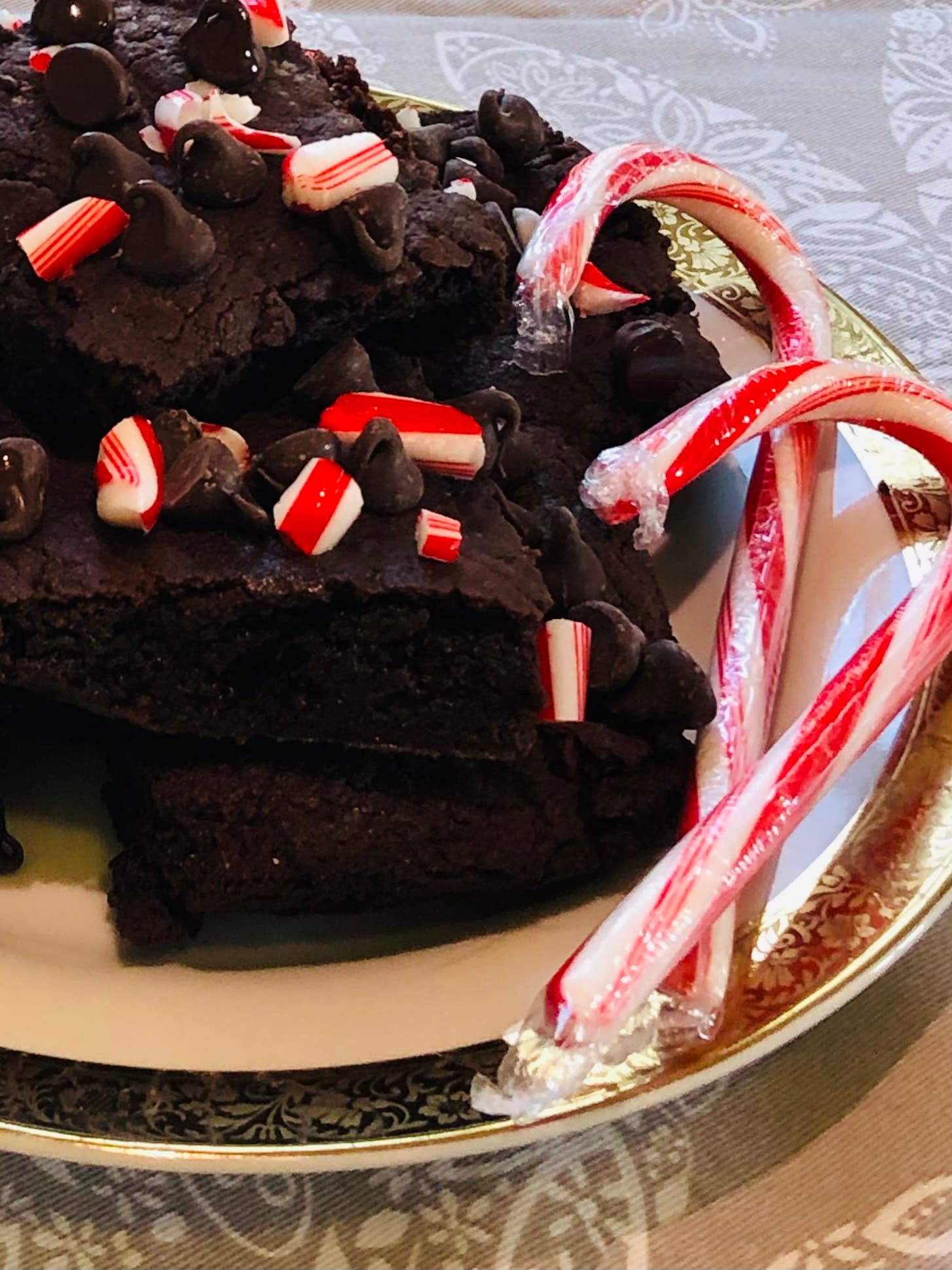 A plate of chocolate brownies topped with peppermint pieces and chocolate chips, accompanied by candy canes.