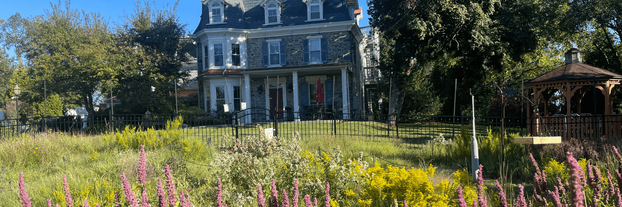 A large historic house surrounded by a vibrant garden and gazebo. A large historic house surrounded by a vibrant garden and gazebo.