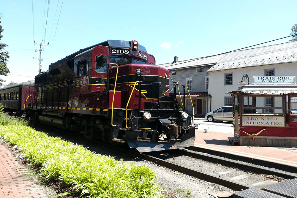 A vintage red train is parked near a station with a sign for train ride information.