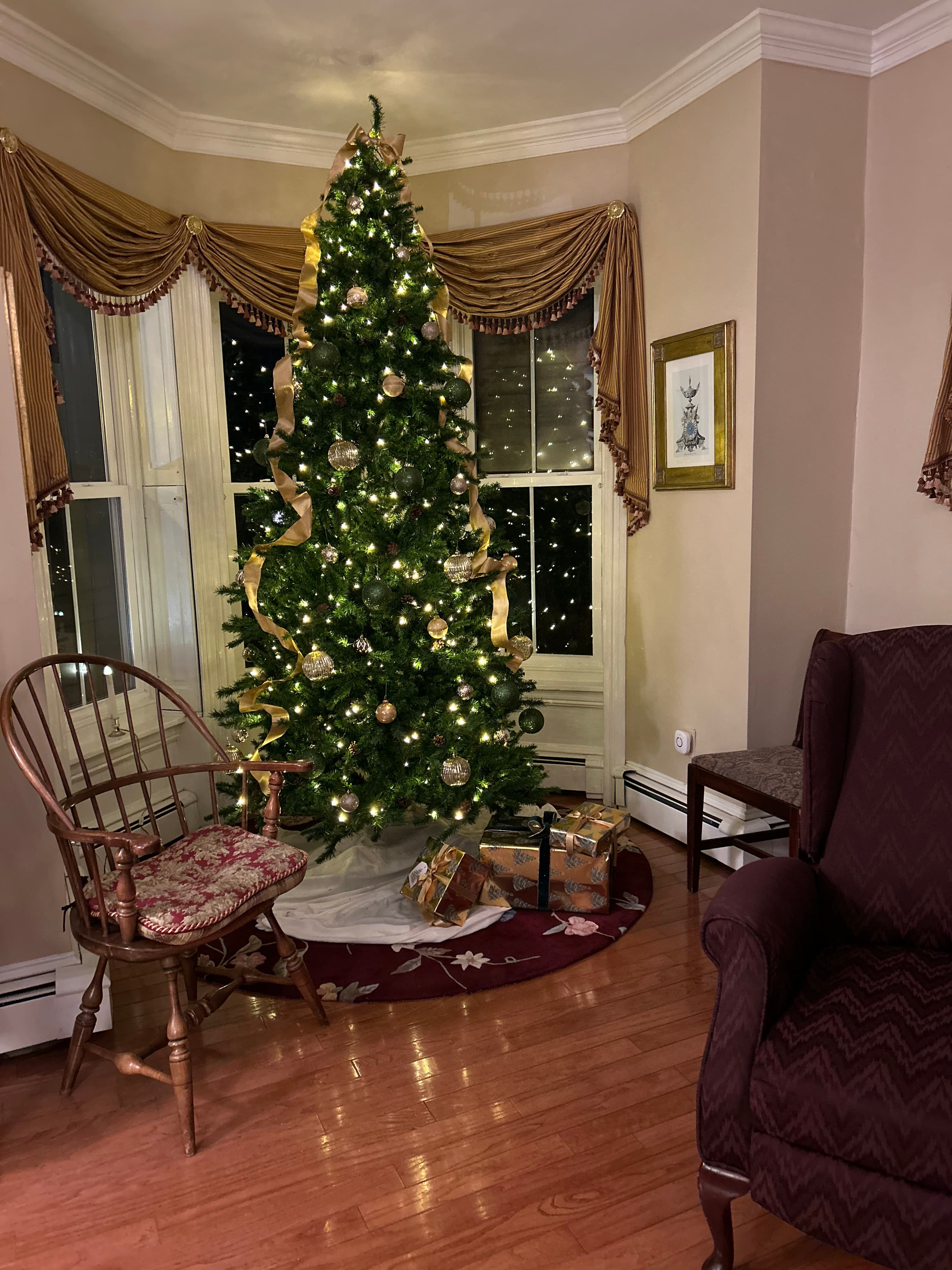 A beautifully decorated Christmas tree with lights and ornaments stands in a cozy living room corner, surrounded by gifts.