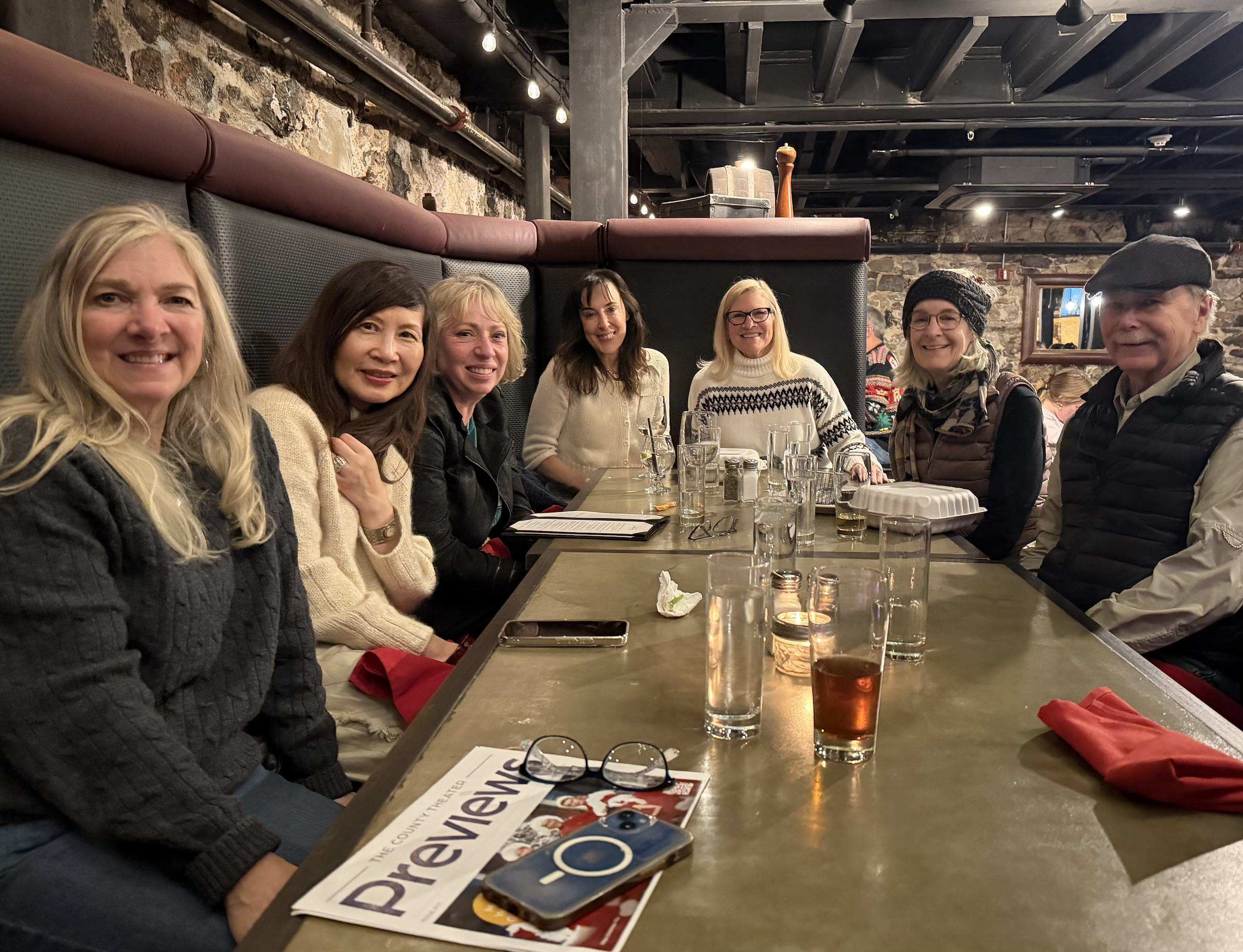 A group of seven people sit around a table in a cozy restaurant, smiling and chatting.