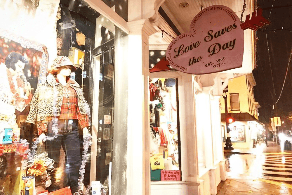 A colorful storefront displays a mannequin in eclectic clothing beneath a sign that reads "Love Saves the Day."