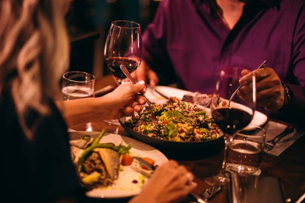 A close-up of a dinner setting with two people enjoying food and wine at a table.