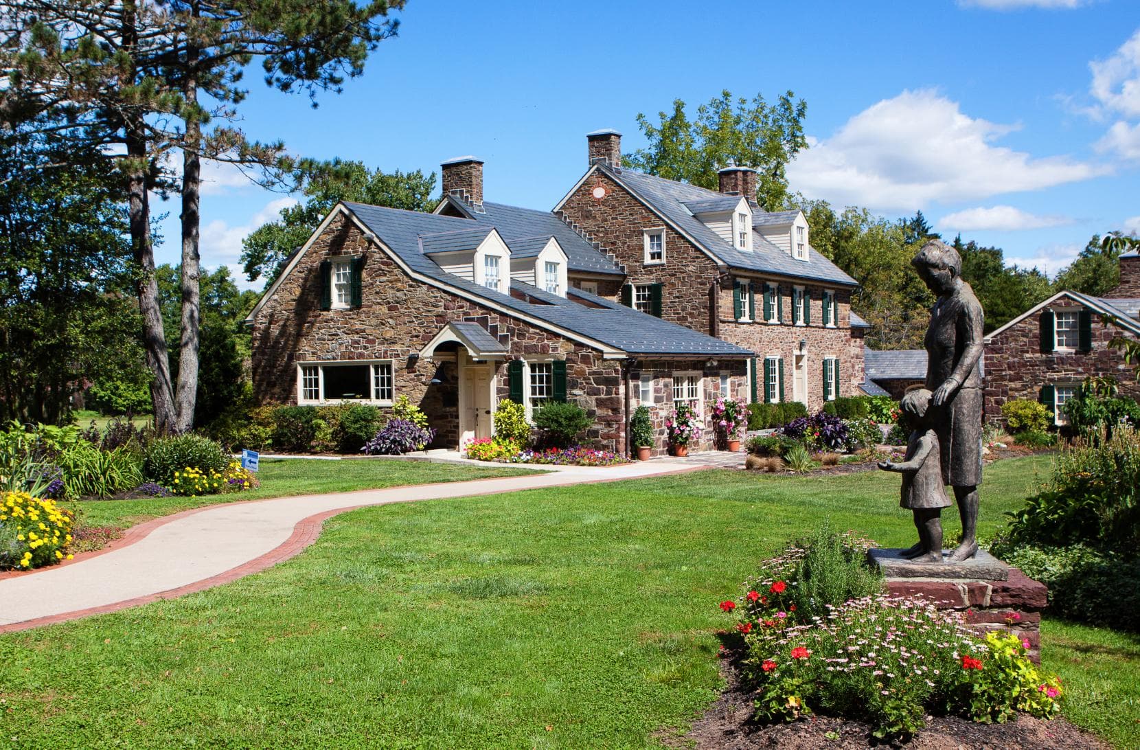 A stone house with a landscaped garden and a statue of a girl holding hands with a woman.