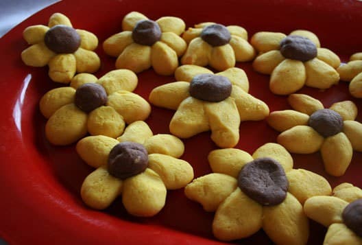 A red plate filled with yellow flower-shaped cookies with brown centers.