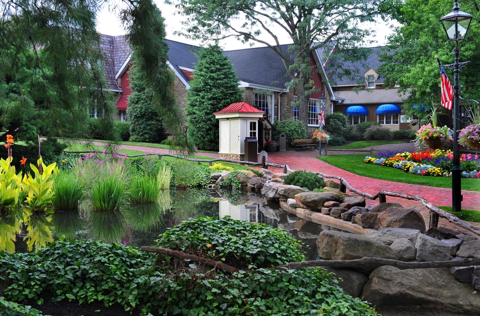 A tranquil garden scene featuring a pond, blooming flowers, and charming buildings.