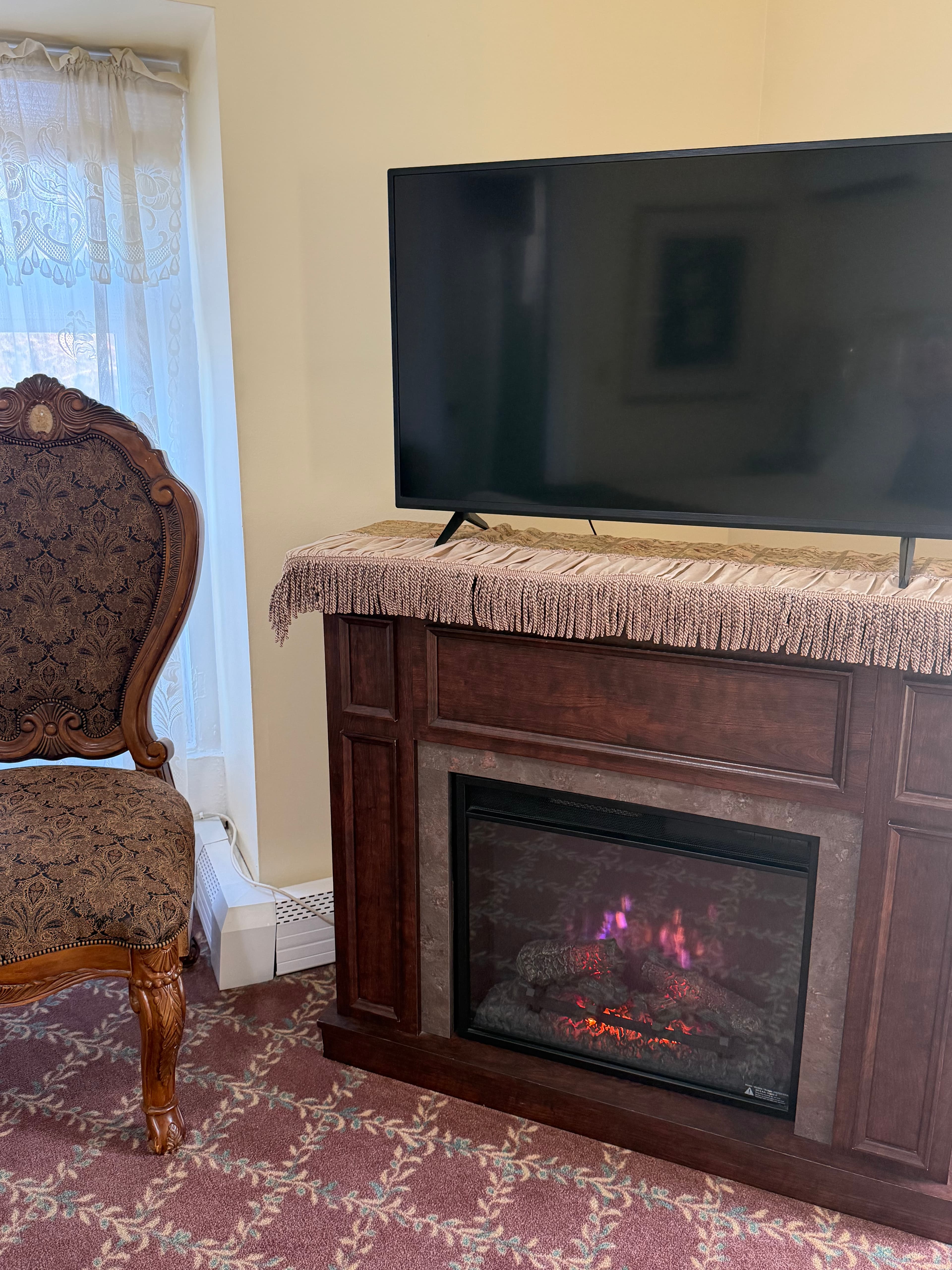 View of electric fireplace, TV, window with chair