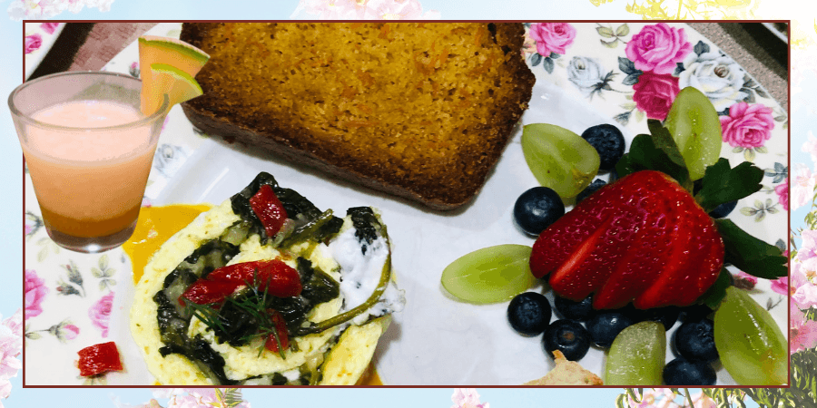 A colorful breakfast plate featuring a vegetable omelet, a slice of bread, fresh fruit, and a glass of pink beverage.