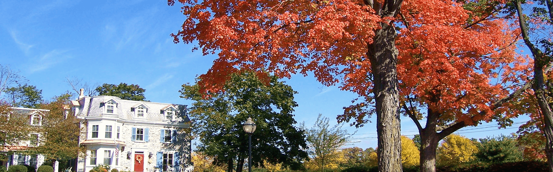 A historic house surrounded by vibrant autumn foliage against a clear blue sky.