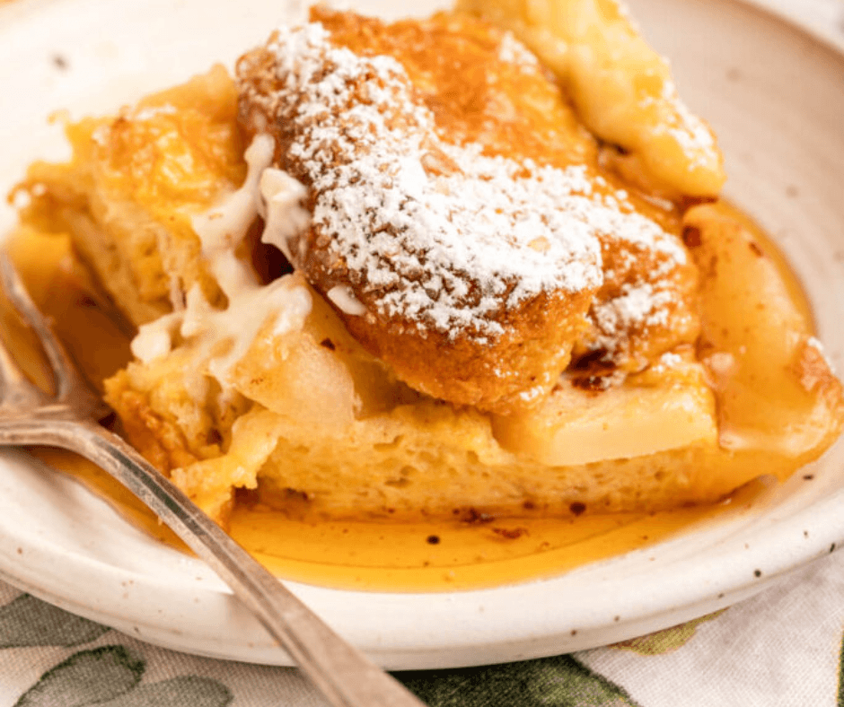 A slice of bread pudding topped with powdered sugar and caramel sauce on a plate with a fork. A slice of bread pudding topped with powdered sugar and caramel sauce on a plate with a fork.