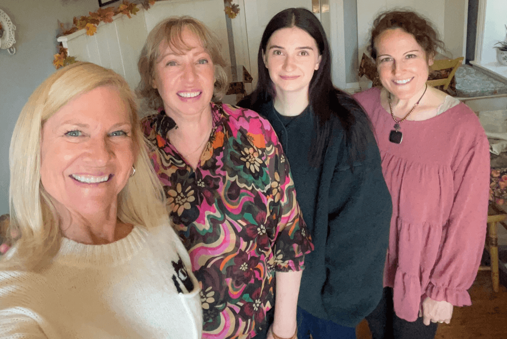 A group of four women smiling together indoors.