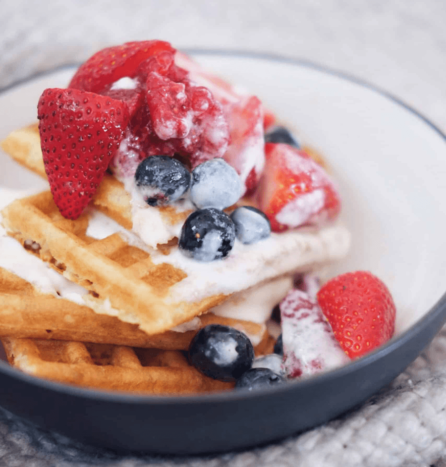 A bowl of waffles topped with fresh strawberries, blueberries, raspberries, and creamy sauce.