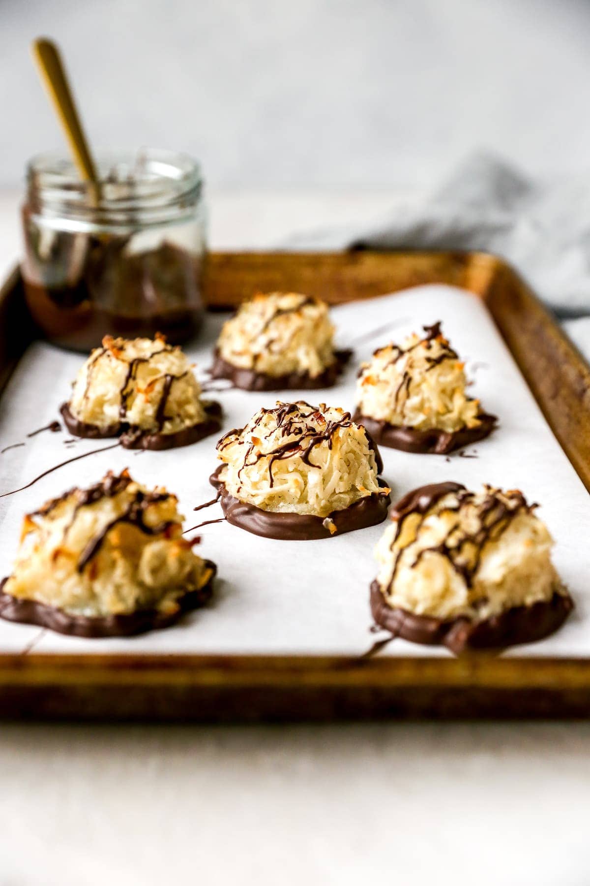 Coconut macaroons dipped in chocolate, drizzled with dark chocolate, on a parchment-lined tray.