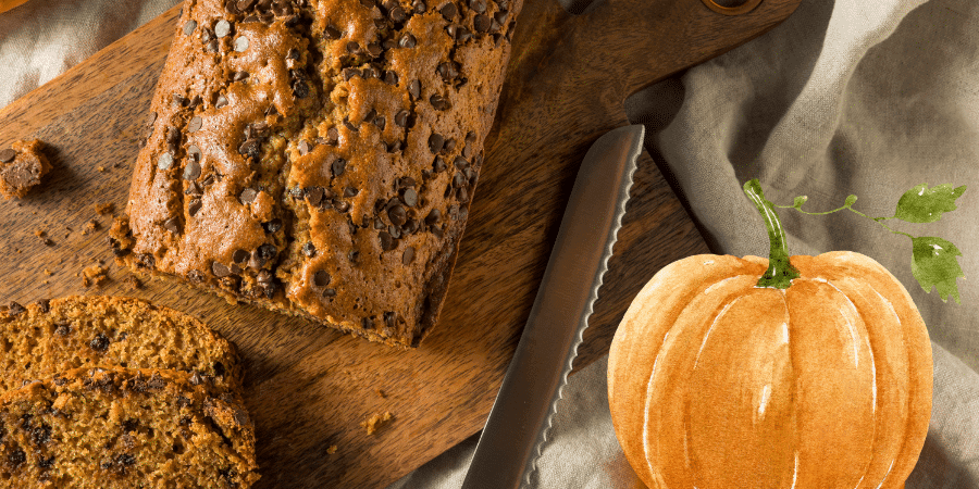 A loaf of chocolate chip pumpkin bread on a wooden cutting board next to a pumpkin illustration.