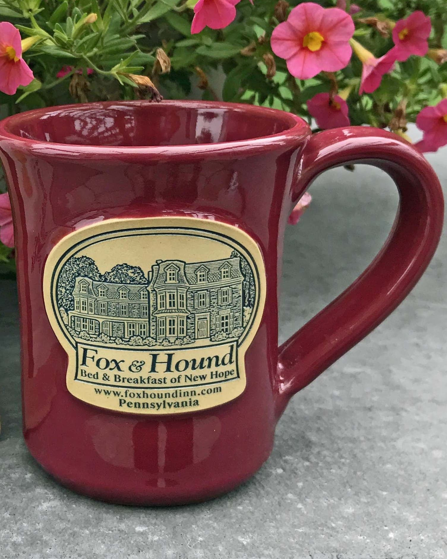 A maroon coffee mug featuring a label for "Fox & Hound Bed & Breakfast of New Hope" with an illustration of a building.