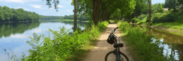 A bicycle rests on a dirt path by a tranquil river surrounded by lush greenery.