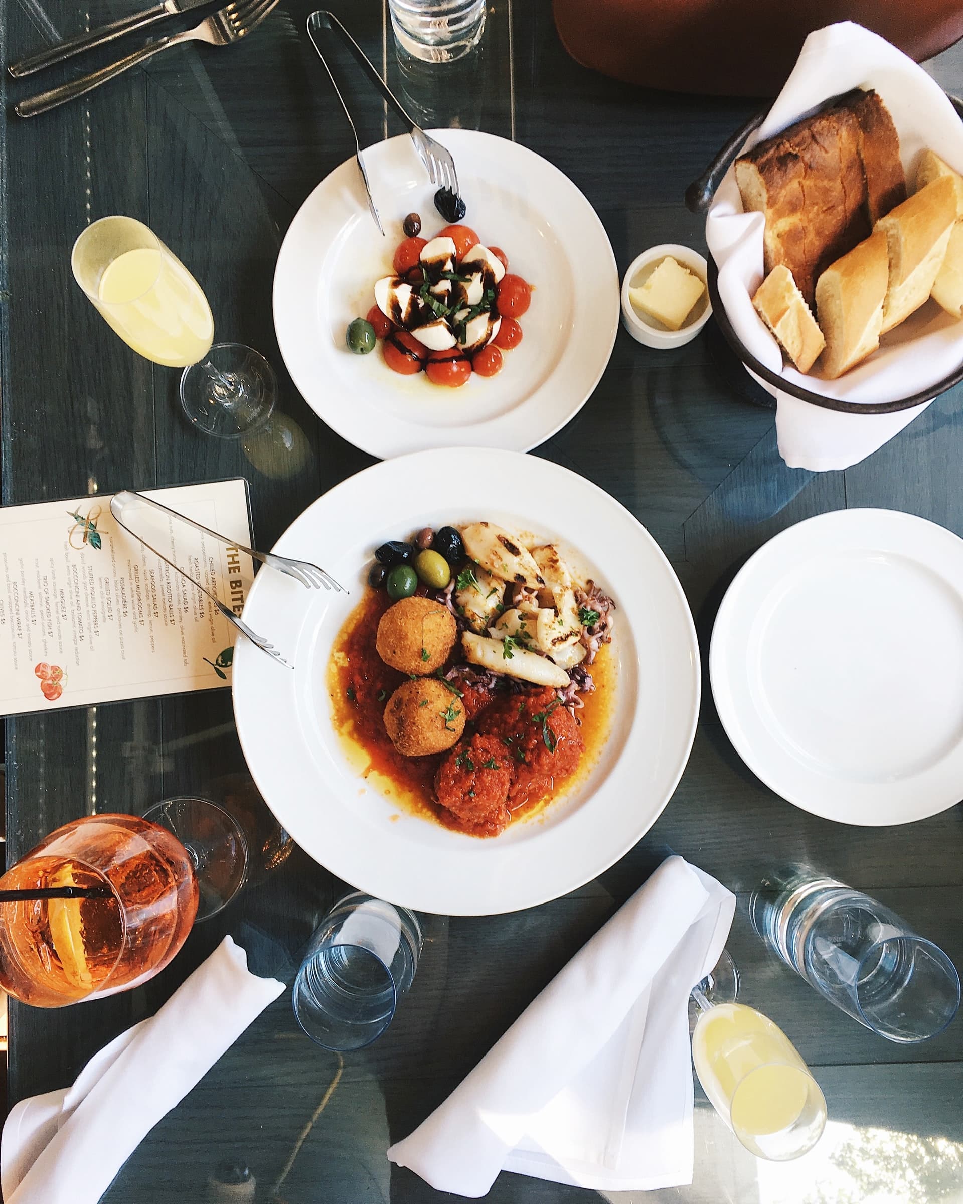 A vibrant table setting featuring a main dish with seafood, vegetables, and two round patties, accompanied by a side salad and bread.