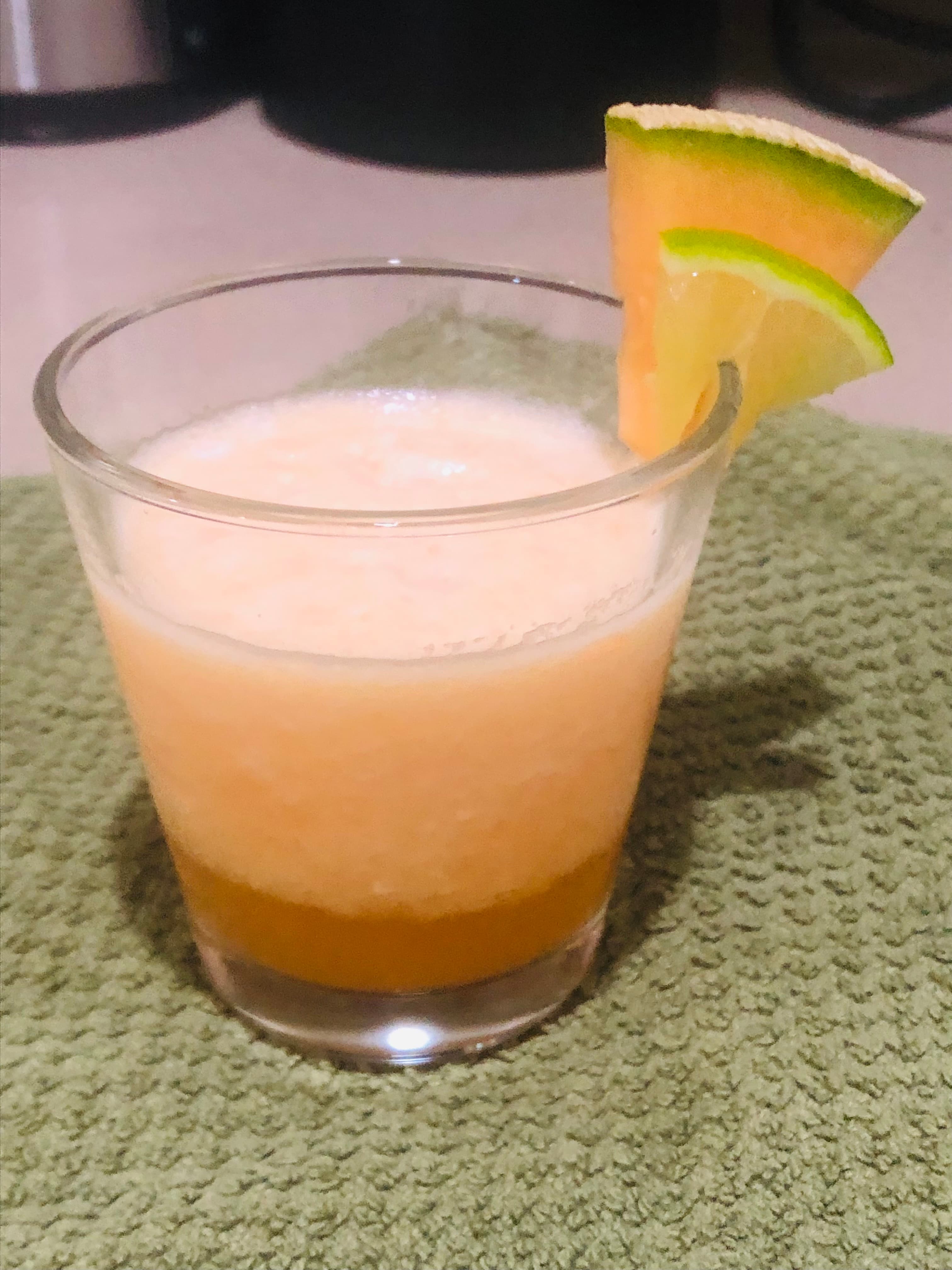 A glass of blended fruit juice with a slice of lime garnish on a green towel.