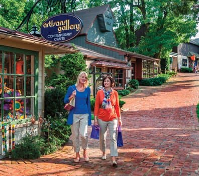 Two women walk along a brick-paved path by shops in a quaint outdoor shopping area.