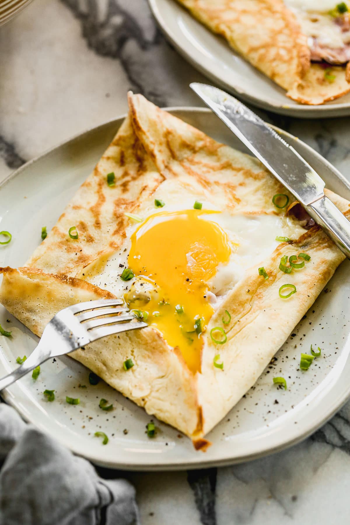 A plate of crepes folded around a sunny-side-up egg, garnished with chopped green onions and pepper.